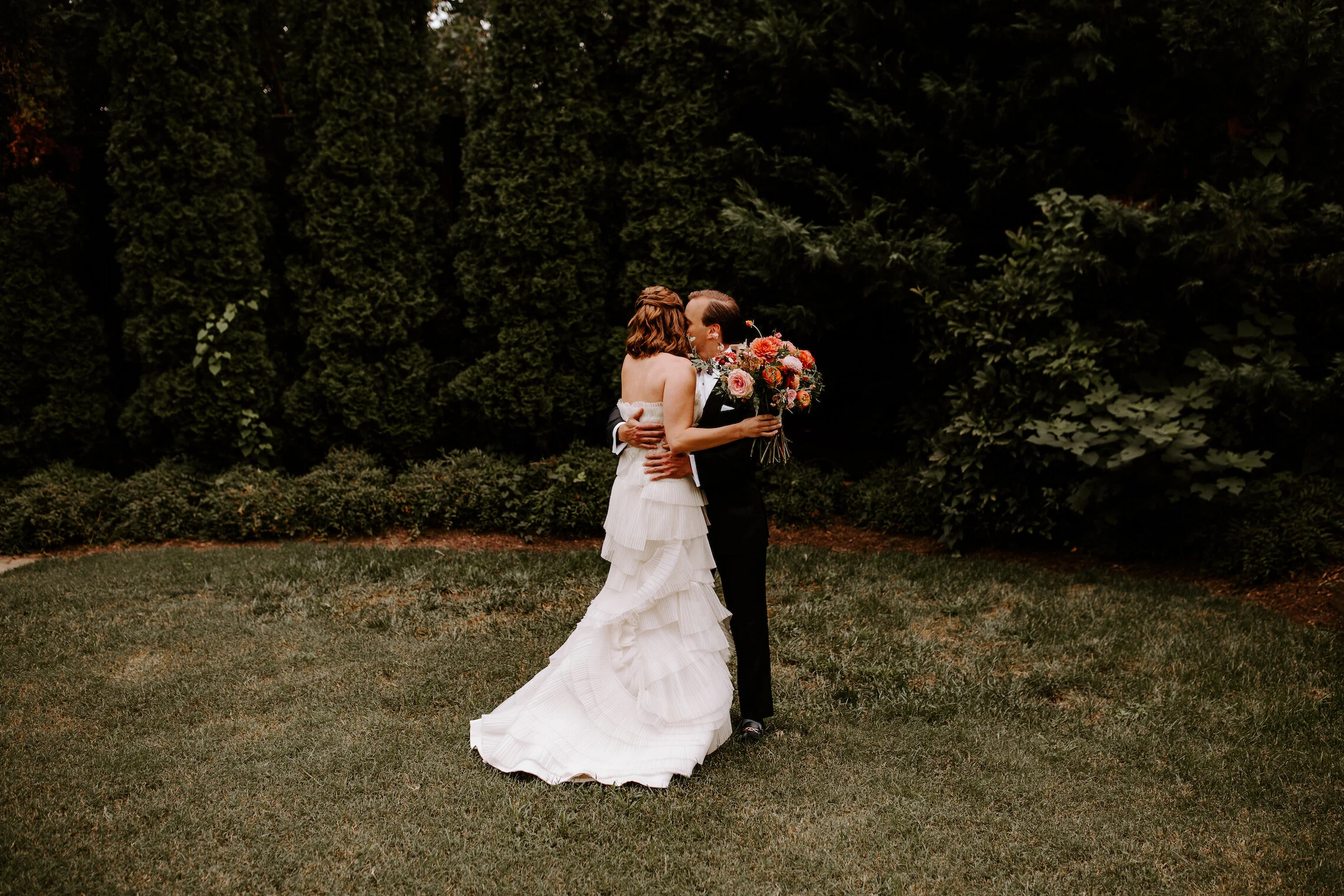 The happiest late summer bridal bouquet overflowing with blooms. This bouquet is filled with coral zinnias, fuchsia and blush dahlias, tangerine ranunculus, petal-heavy roses, pink snowberry, and touches of smilax vine. Designed by Nashville wedding…