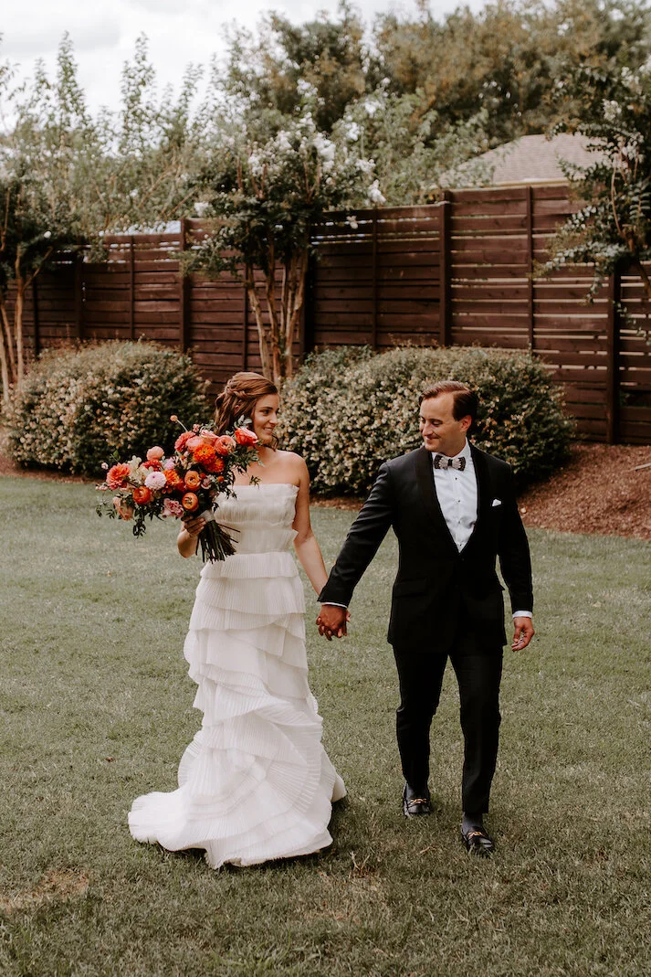 The happiest late summer bridal bouquet overflowing with blooms. This bouquet is filled with coral zinnias, fuchsia and blush dahlias, tangerine ranunculus, petal-heavy roses, pink snowberry, and touches of smilax vine. Designed by Nashville wedding…