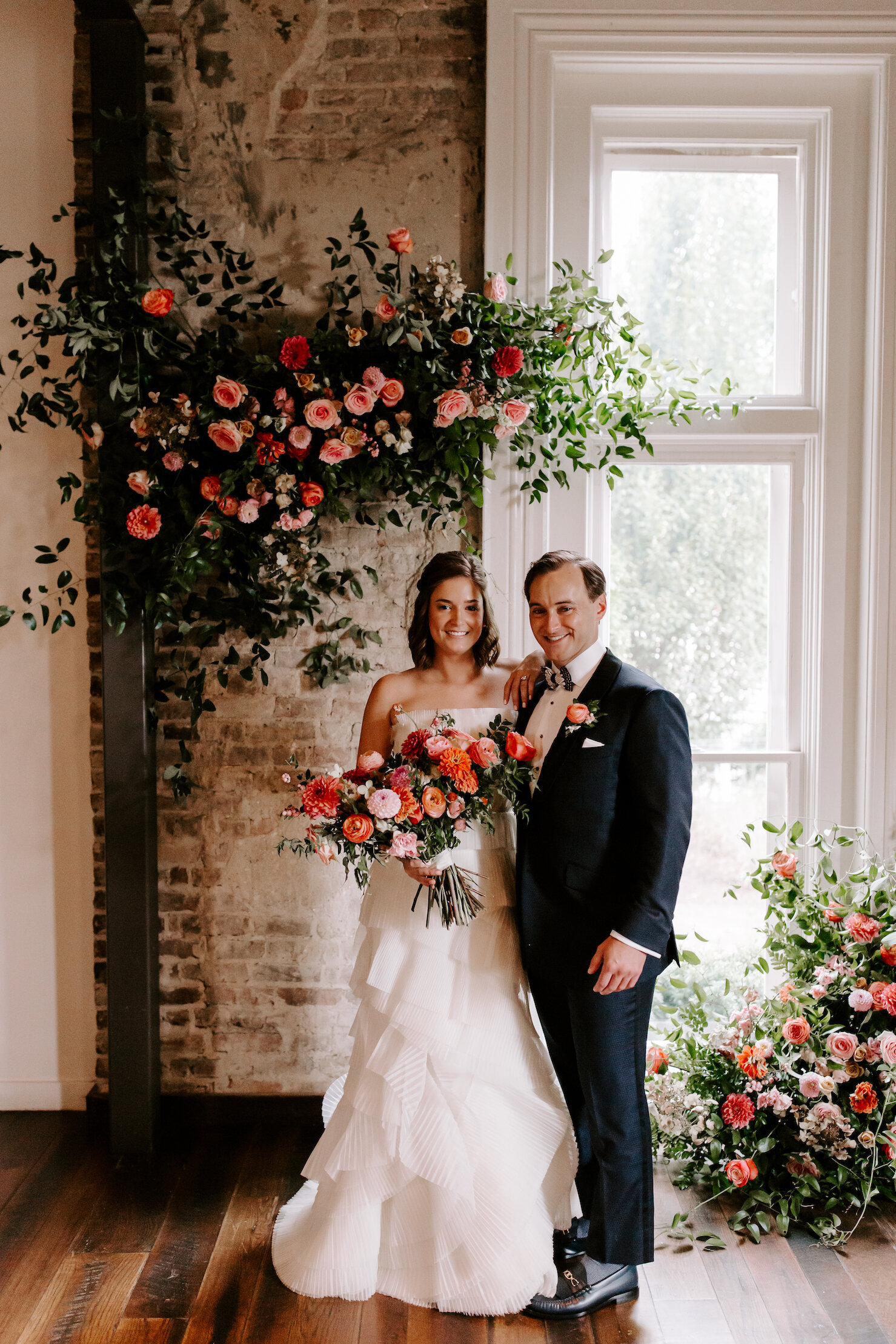 This wedding featured a stunning ceremony arch and a moss and floral wall installation. Blooms used were coral zinnias, fuchsia and blush dahlias, tangerine ranunculus, petal-heavy roses, pink snowberry, and sprawling smilax vine. Designed by Nashvi…