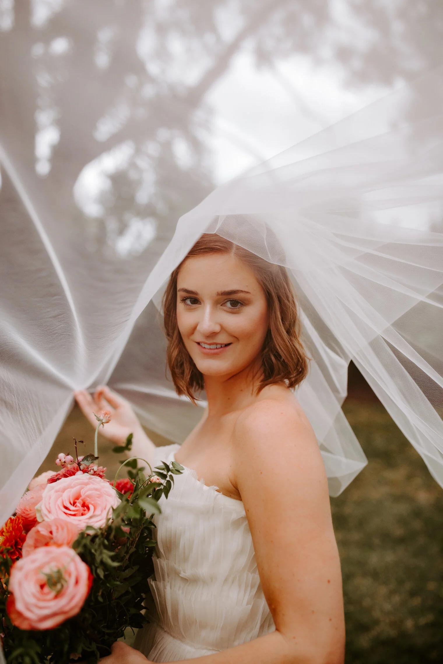 The happiest late summer bridal bouquet overflowing with blooms. This bouquet is filled with coral zinnias, fuchsia and blush dahlias, tangerine ranunculus, petal-heavy roses, pink snowberry, and touches of smilax vine. Designed by Nashville wedding…