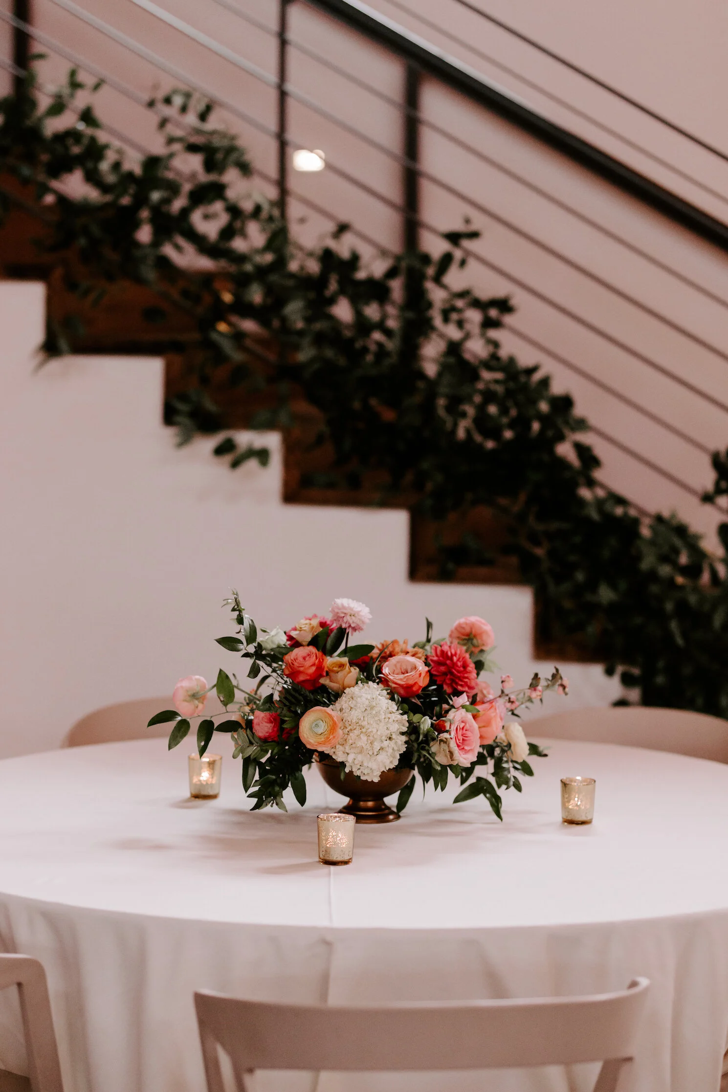 Bright and summery centerpieces filled with coral zinnias, fuchsia and blush dahlias, tangerine ranunculus, petal-heavy roses, pink snowberry, fluffy hydrangea, and sprawling smilax vine. Designed by Nashville wedding floral designer, Rosemary & Fin…