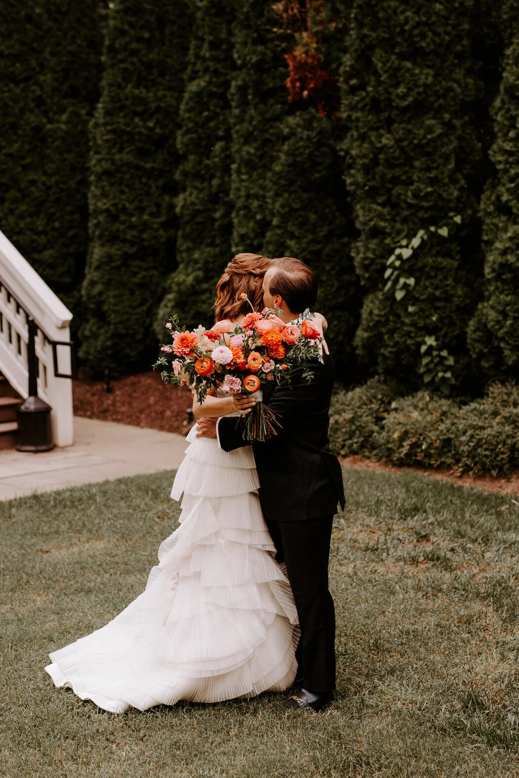 The happiest late summer bridal bouquet overflowing with blooms. This bouquet is filled with coral zinnias, fuchsia and blush dahlias, tangerine ranunculus, petal-heavy roses, pink snowberry, and touches of smilax vine. Designed by Nashville wedding…