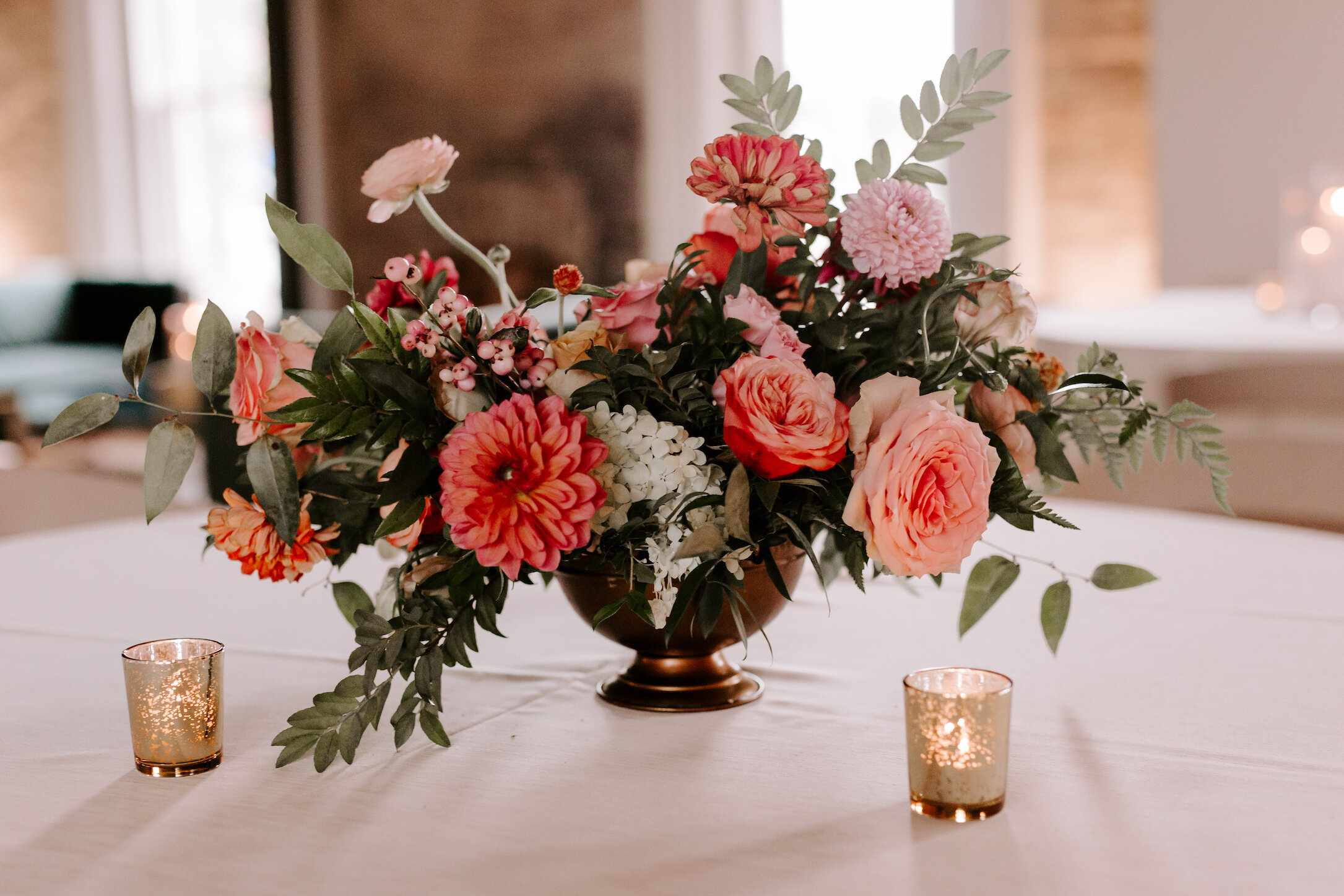 Bright and summery centerpieces filled with coral zinnias, fuchsia and blush dahlias, tangerine ranunculus, petal-heavy roses, pink snowberry, fluffy hydrangea, and sprawling smilax vine. Designed by Nashville wedding floral designer, Rosemary & Fin…