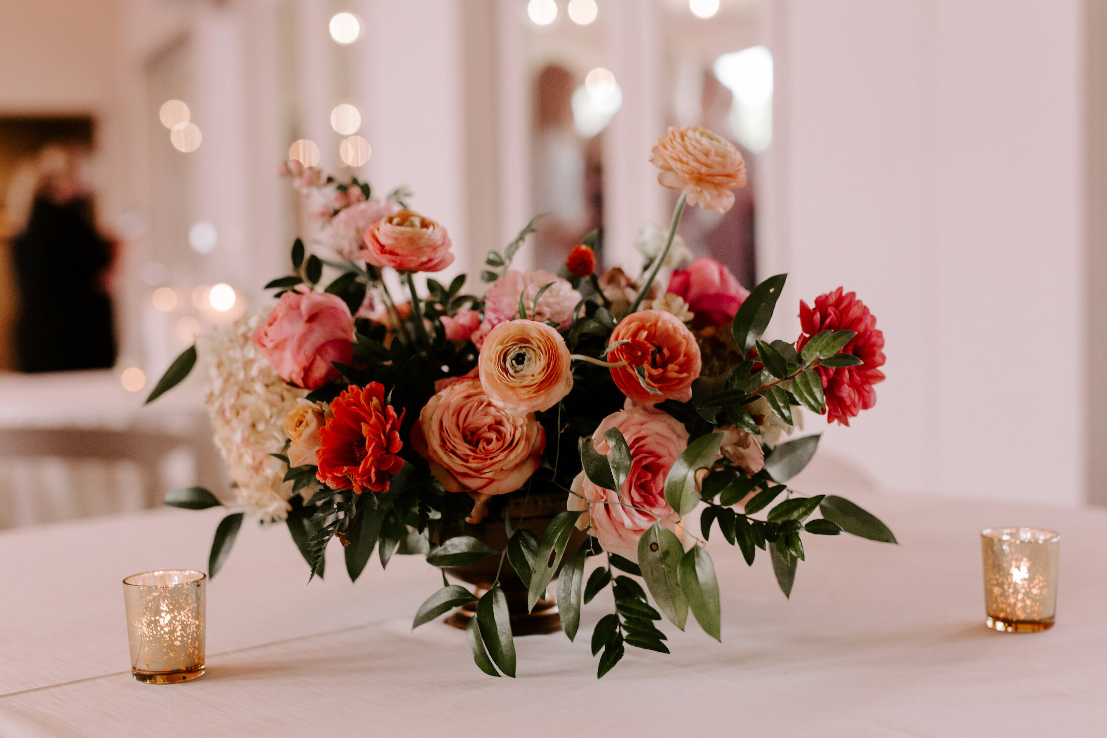 Bright and summery centerpieces filled with coral zinnias, fuchsia and blush dahlias, tangerine ranunculus, petal-heavy roses, pink snowberry, fluffy hydrangea, and sprawling smilax vine. Designed by Nashville wedding floral designer, Rosemary & Fin…