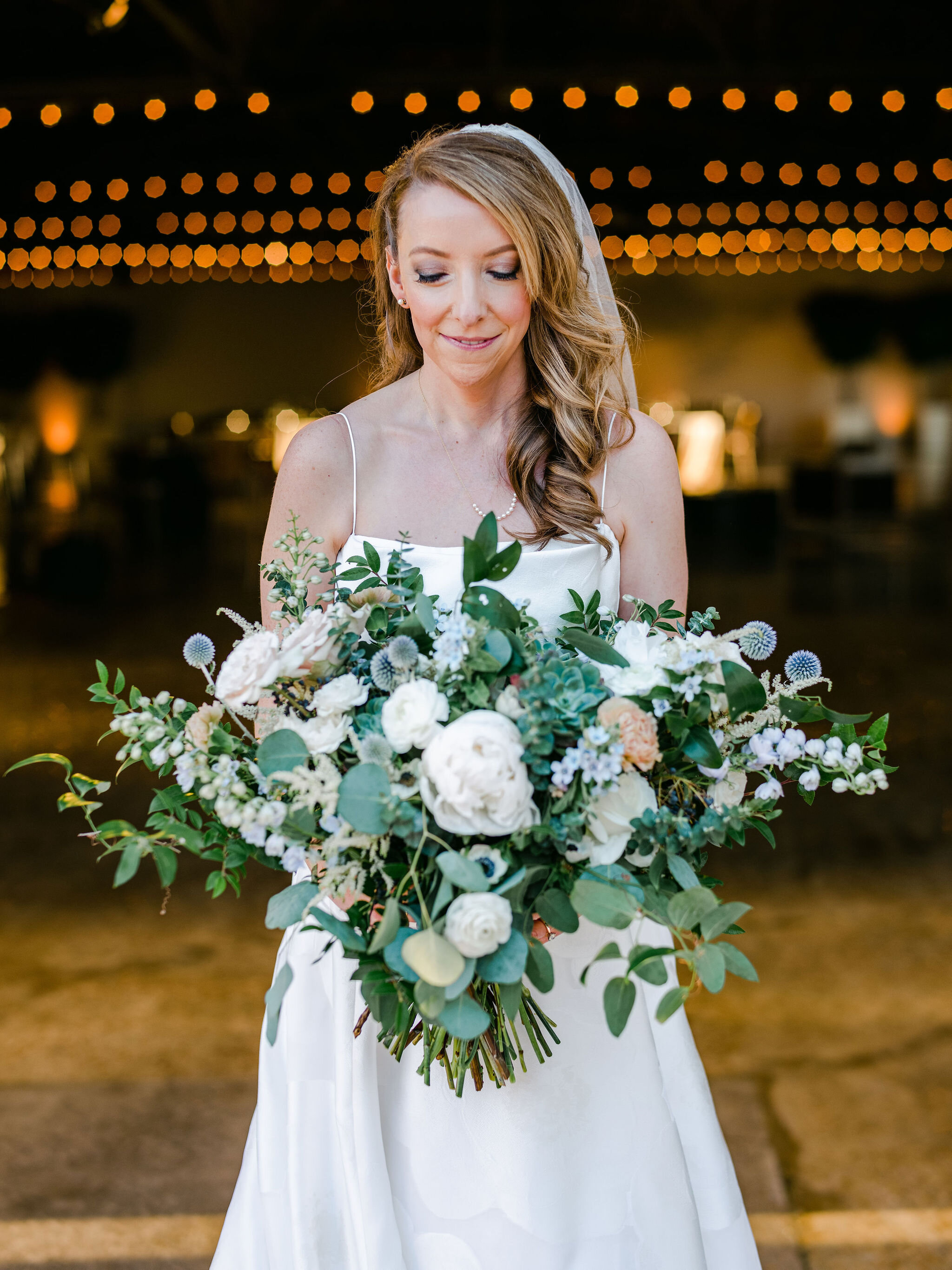 A lush and sprawling bridal bouquet filled to the brim. Blush and white garden roses, white peonies, blue thistle, delphinium, blue tweedia, white astilbe, white ranunculus, baby and silver dollar eucalyptus, huckleberry, and smilax vine are just so…
