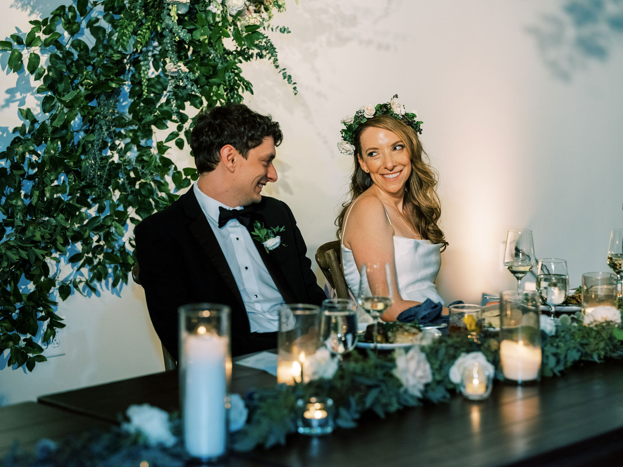This wedding featured lush table garlands filled with blooms of blush and white garden roses, blue globe thistle, privet berry, seeded eucalyptus and lush greenery. Twinkly pillar candles and votives were scattered throughout the garland. Designed b…