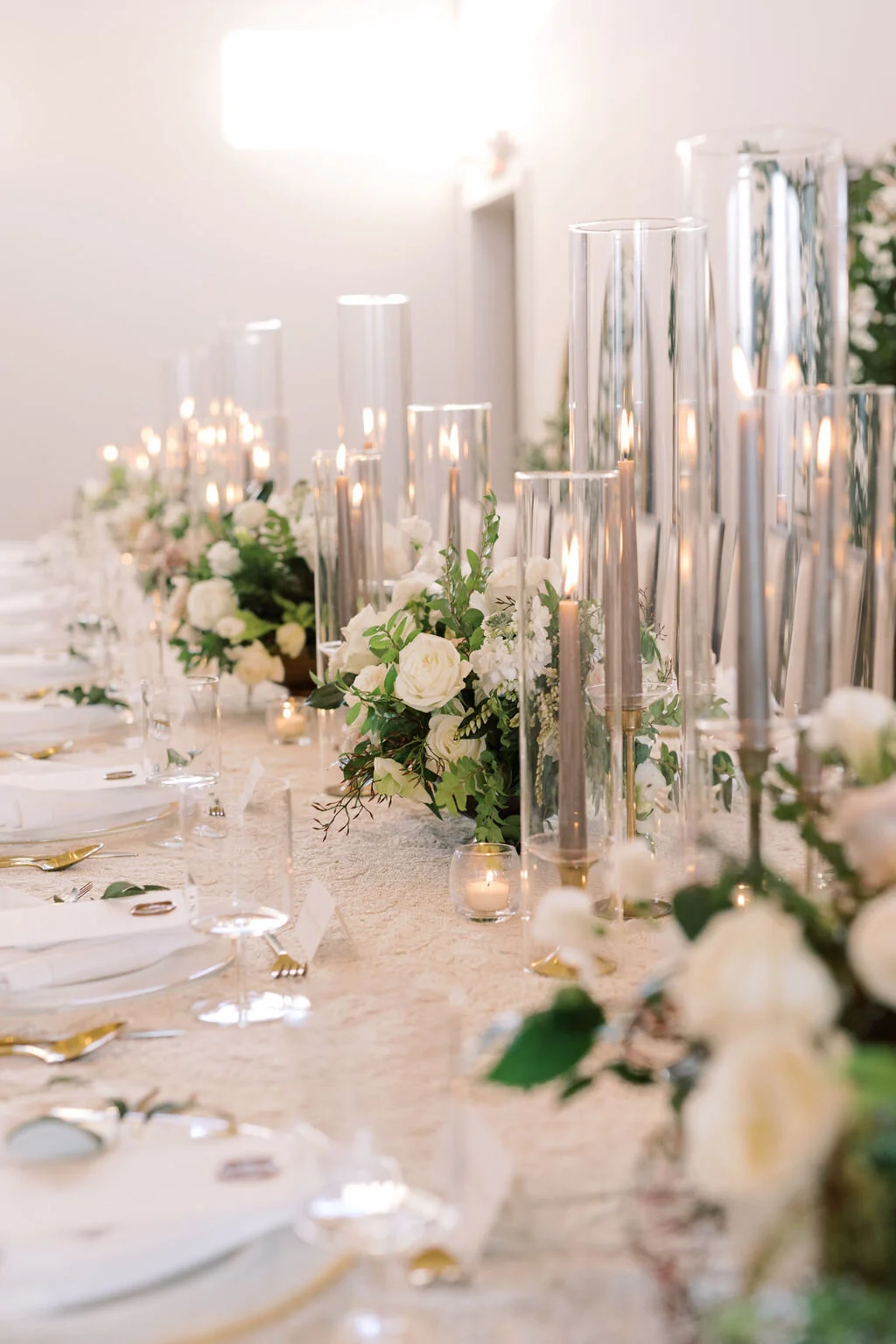 This twinkling reception is filled with taupe tapers in collected brass candlesticks. Centerpieces filled with delicate blooms of quicksand roses, white ice roses, majolica spray roses, fluffy ranunculus, white stock, delicate sweet pea and natural …