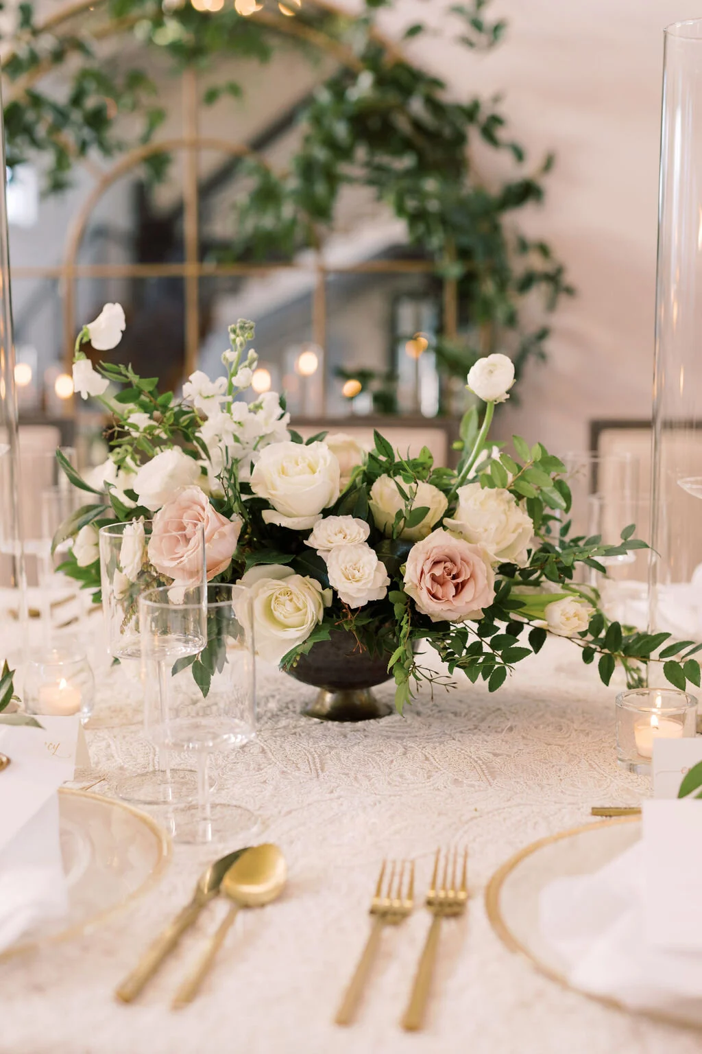 This twinkling reception is filled with taupe tapers in collected brass candlesticks. Centerpieces filled with delicate blooms of quicksand roses, white ice roses, majolica spray roses, fluffy ranunculus, white stock, delicate sweet pea and natural …