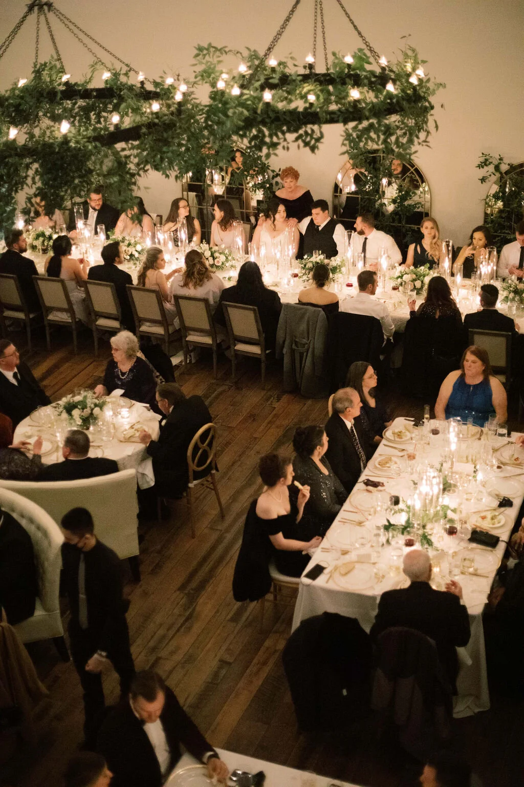 This twinkling reception is filled with taupe tapers in collected brass candlesticks. Wild green chandeliers float over centerpieces filled with delicate blooms of quicksand roses, white ice roses, majolica spray roses, fluffy ranunculus, white stoc…
