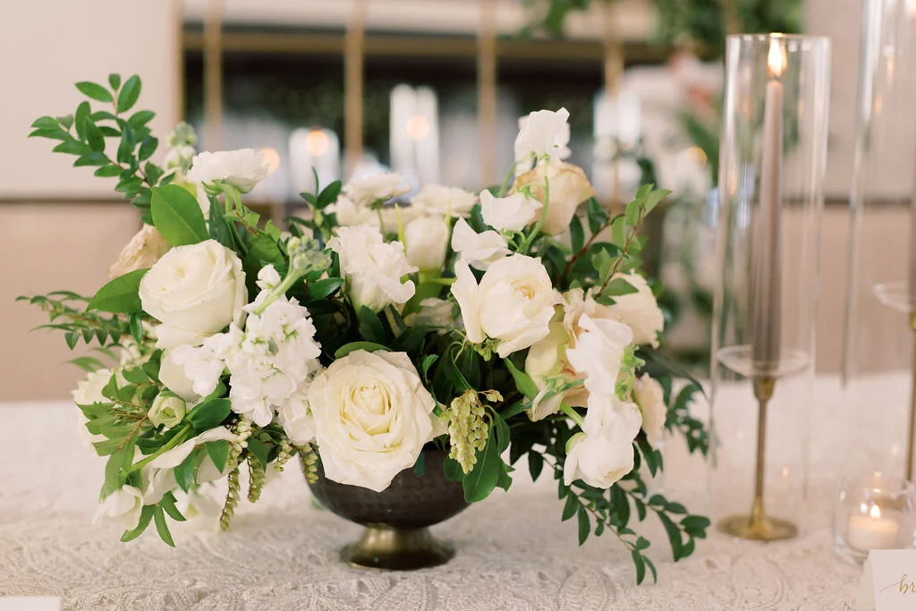 This twinkling reception is filled with taupe tapers in collected brass candlesticks. Centerpieces filled with delicate blooms of quicksand roses, white ice roses, majolica spray roses, fluffy ranunculus, white stock, delicate sweet pea and natural …