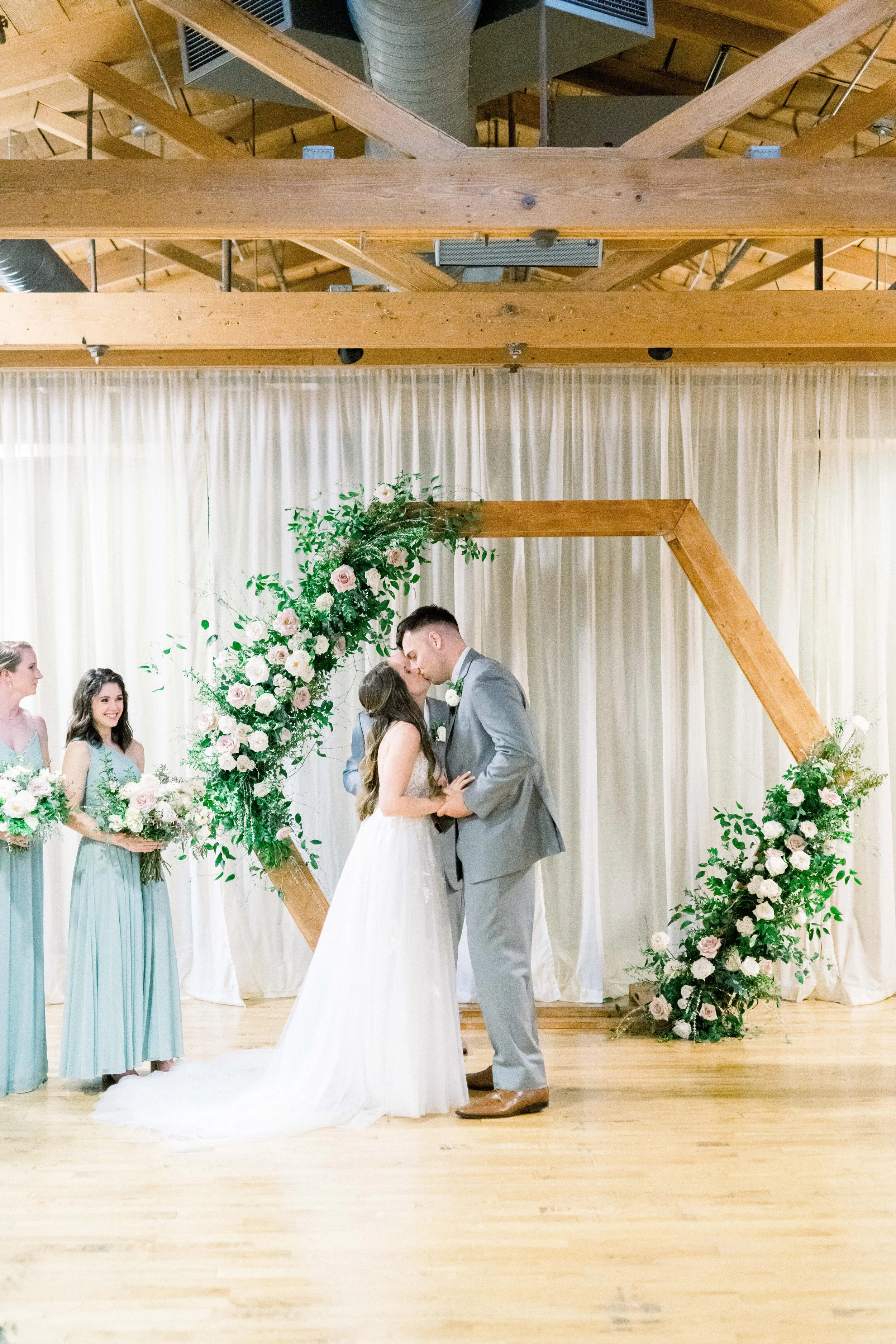 A hexagon arch makes the perfect ceremony backdrop. Blooms used here are blush quicksand roses, cream garden roses, white ranunculus, spray roses, and lush greenery. Designed by florist Rosemary & Finch in Nashville, TN.