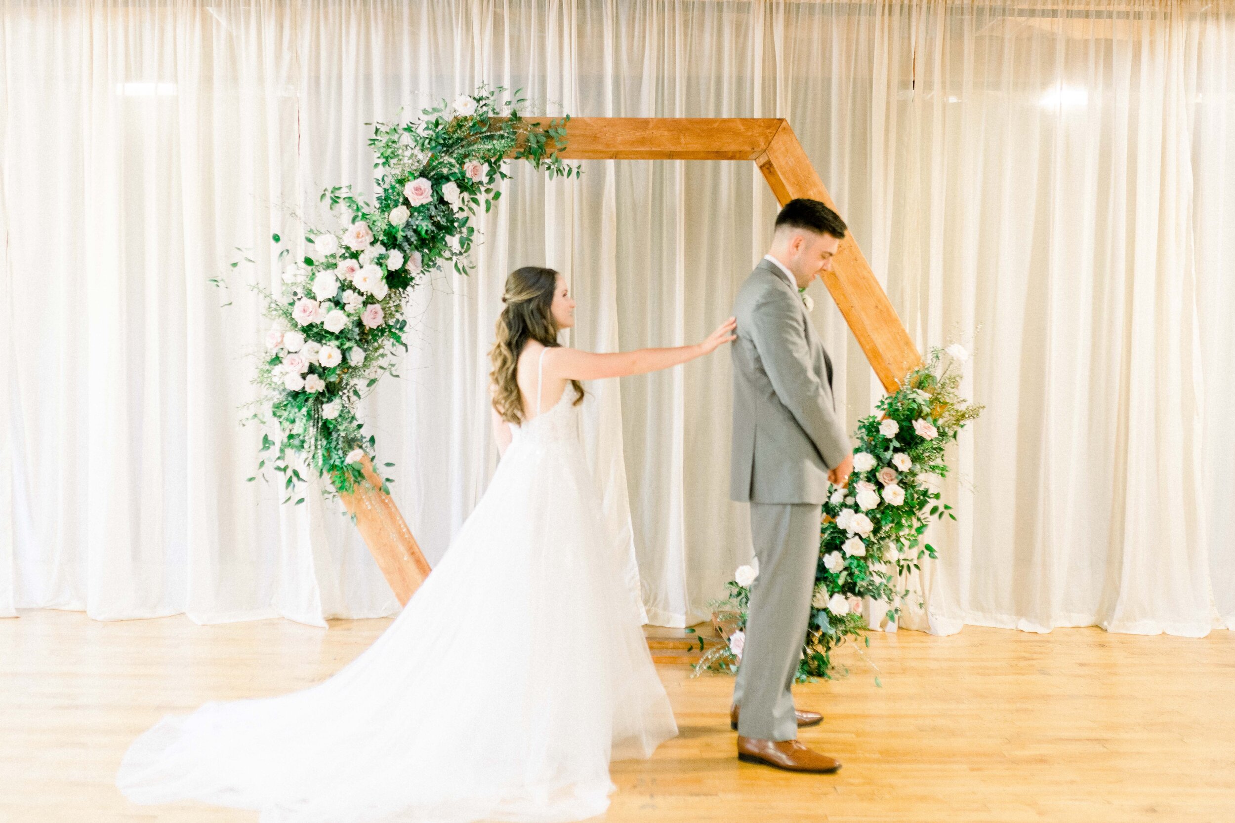 A hexagon arch makes the perfect ceremony backdrop. Blooms used here are blush quicksand roses, cream garden roses, white ranunculus, spray roses, and lush greenery. Designed by florist Rosemary & Finch in Nashville, TN.