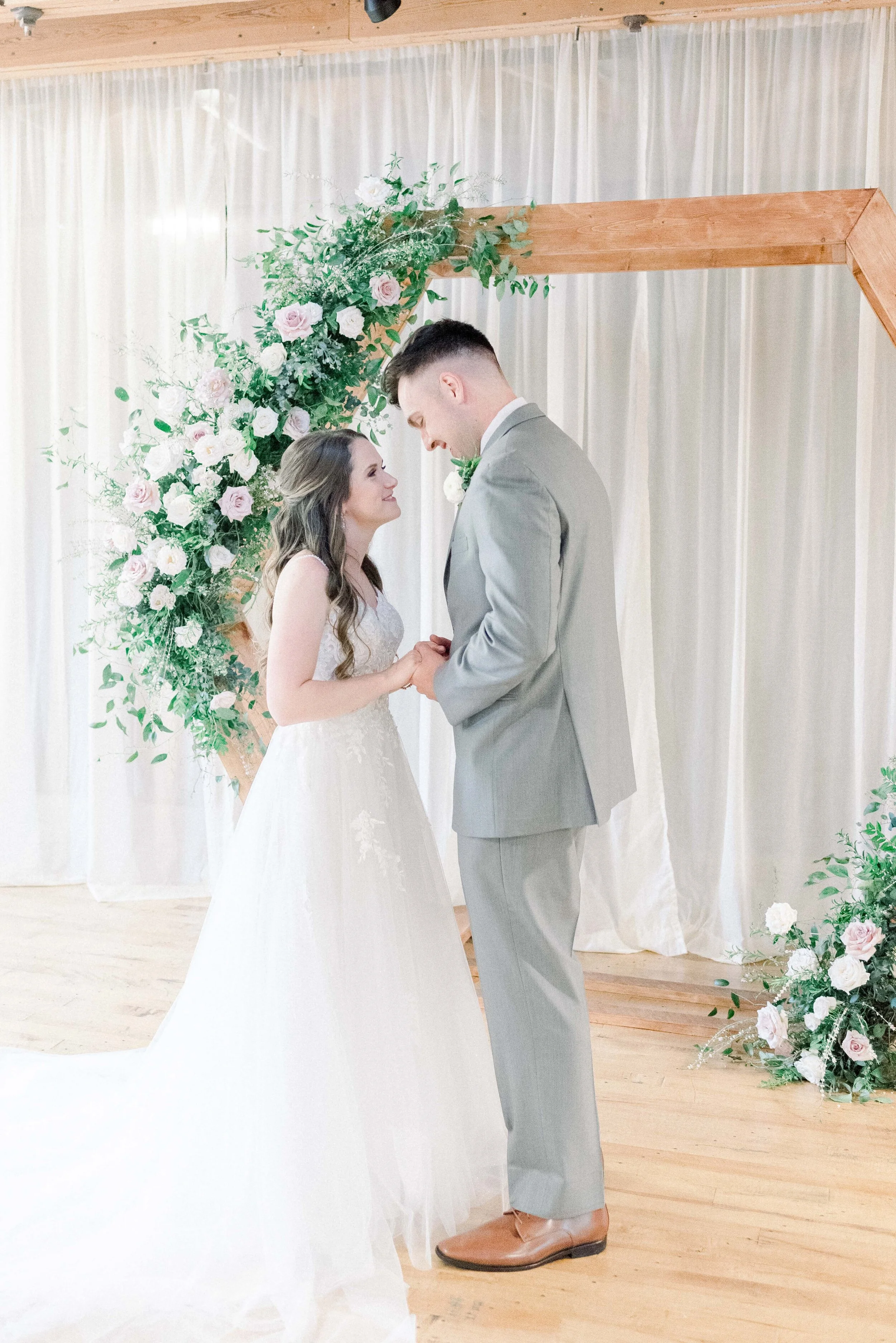 A hexagon arch makes the perfect ceremony backdrop. Blooms used here are blush quicksand roses, cream garden roses, white ranunculus, spray roses, and lush greenery. Designed by florist Rosemary & Finch in Nashville, TN.