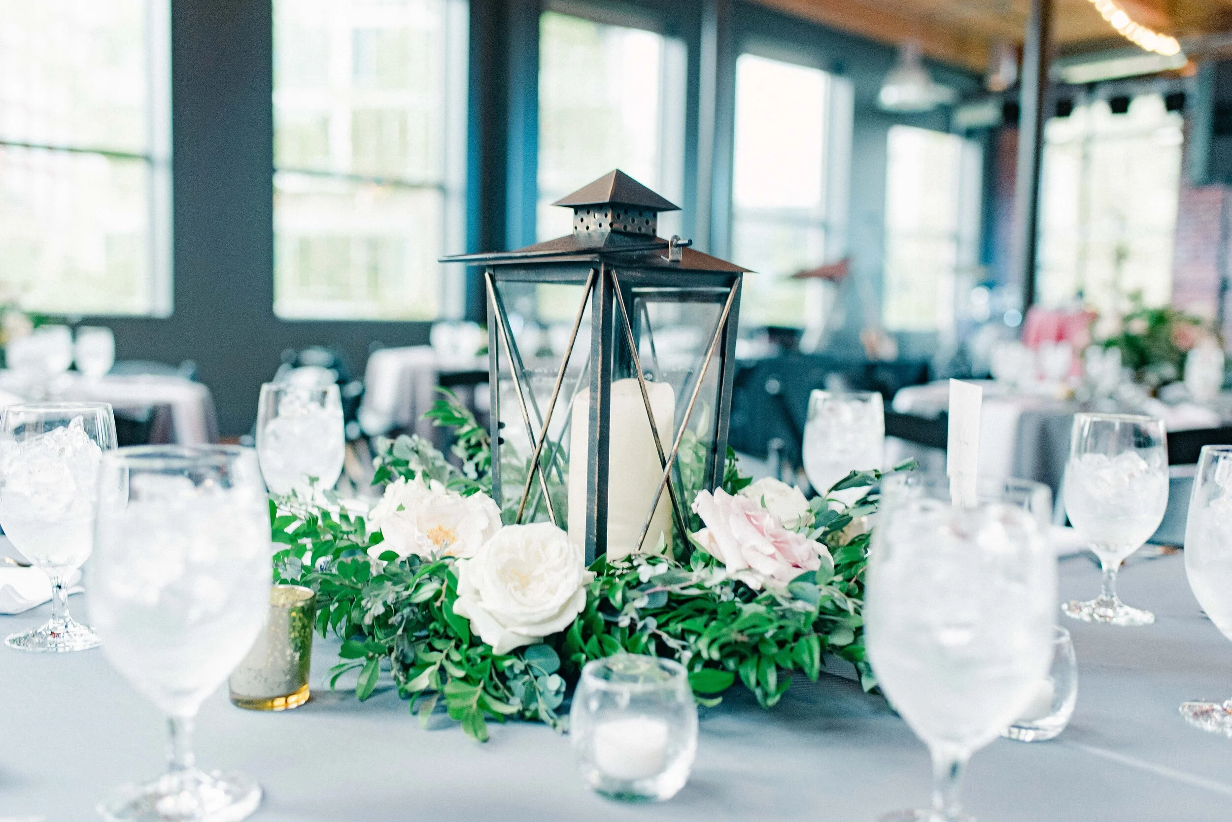 Table decor for this stunning wedding consisted of several different components. Round tables held lanterns adorned with blush and cream roses and lush greenery. Long, farm tables had garlands of eucalyptus and twinkling candles. Centerpieces filled…