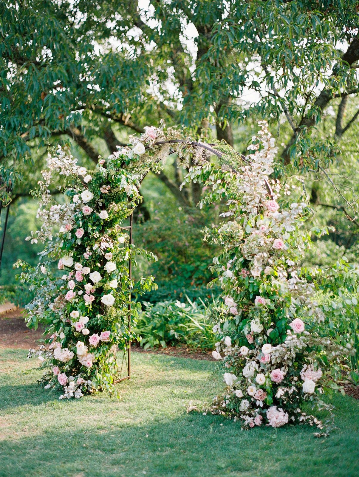 A fairytail arch filled with blush and ivory garden roses, majolica spray roses, champagne roses, eleagnus, and lush sprawling greenery. Designed by Rosemary & Finch in Nashville, TN.