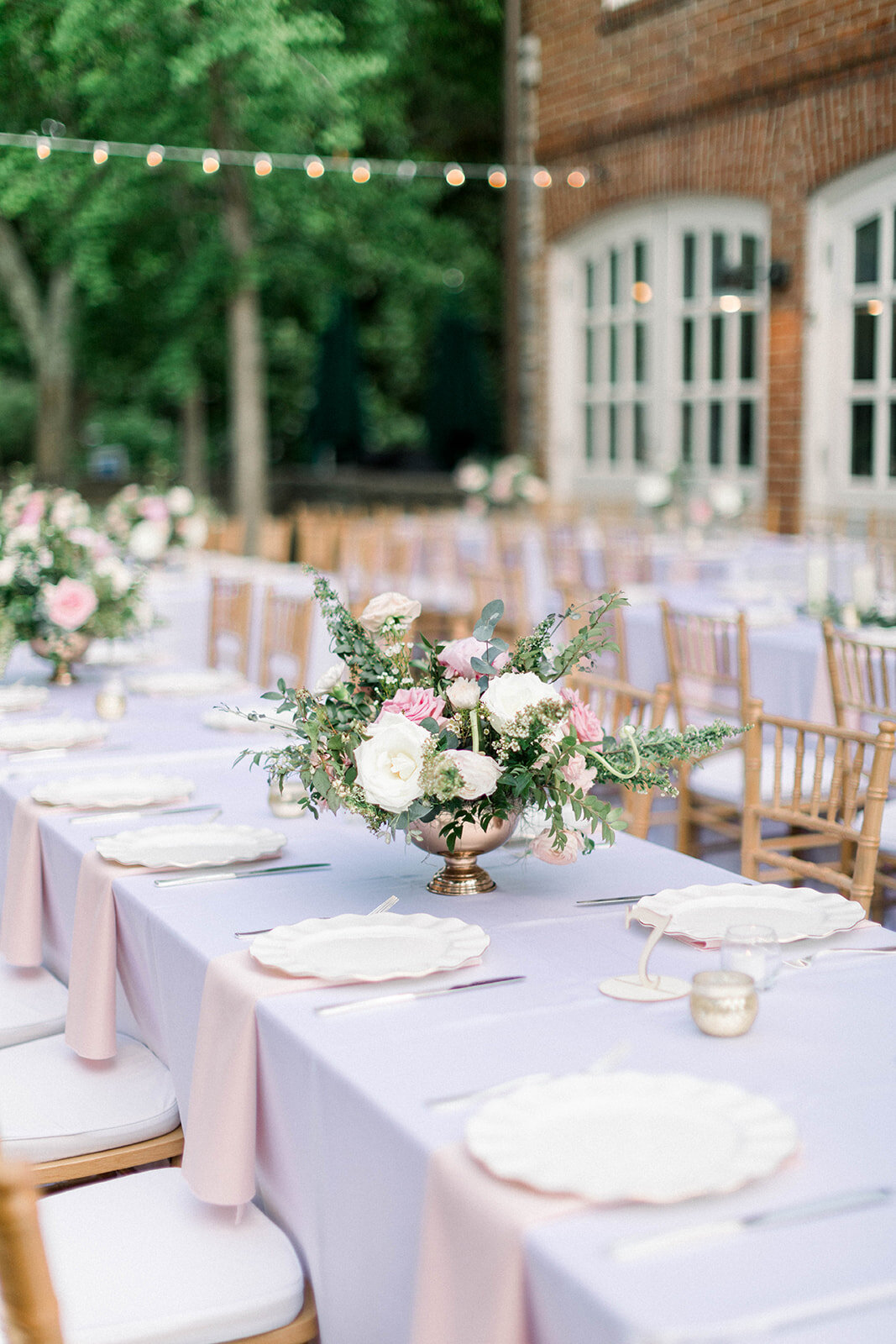 This courtyard reception has eucalyptus garlands filled with blush and white flowers along with centerpieces of pink peonies, ivory garden roses, heirloom carnations, and hydrangea. Designed by Rosemary & Finch in Nashville, TN.