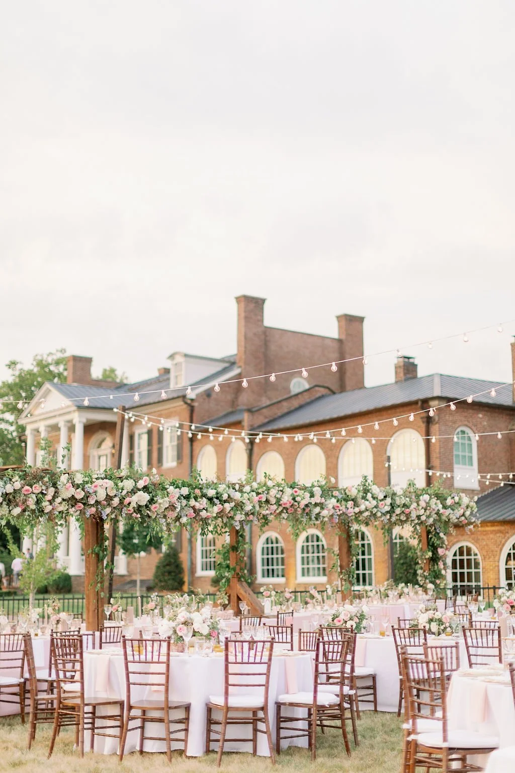 This private estate garden-inspired head table pergola is covered with pink and ivory roses, majolica spray roses, heirloom carnations, blue delphinium, hydrangea and natural greenery. Designed by Rosemary & Finch in Nashville, TN.