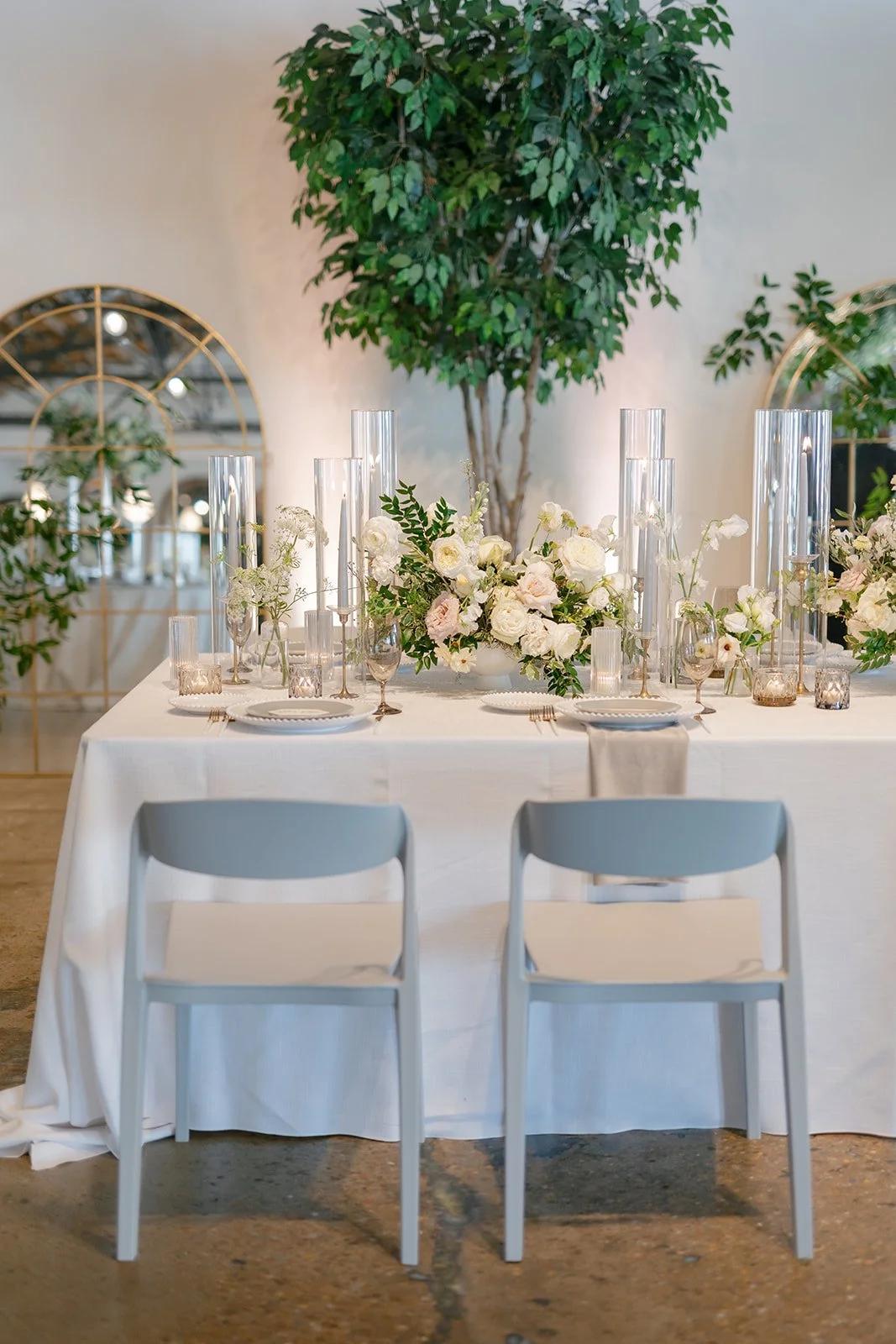 Low floral centerpieces for elegant wedding overflowing with white garden roses, ranunculus, butterfly ranunculus, scabiosa, lisianthus, sweet peas, and natural dark greenery. Floral hues of white, cream, and blush. Designed by Rosemary and Finch in