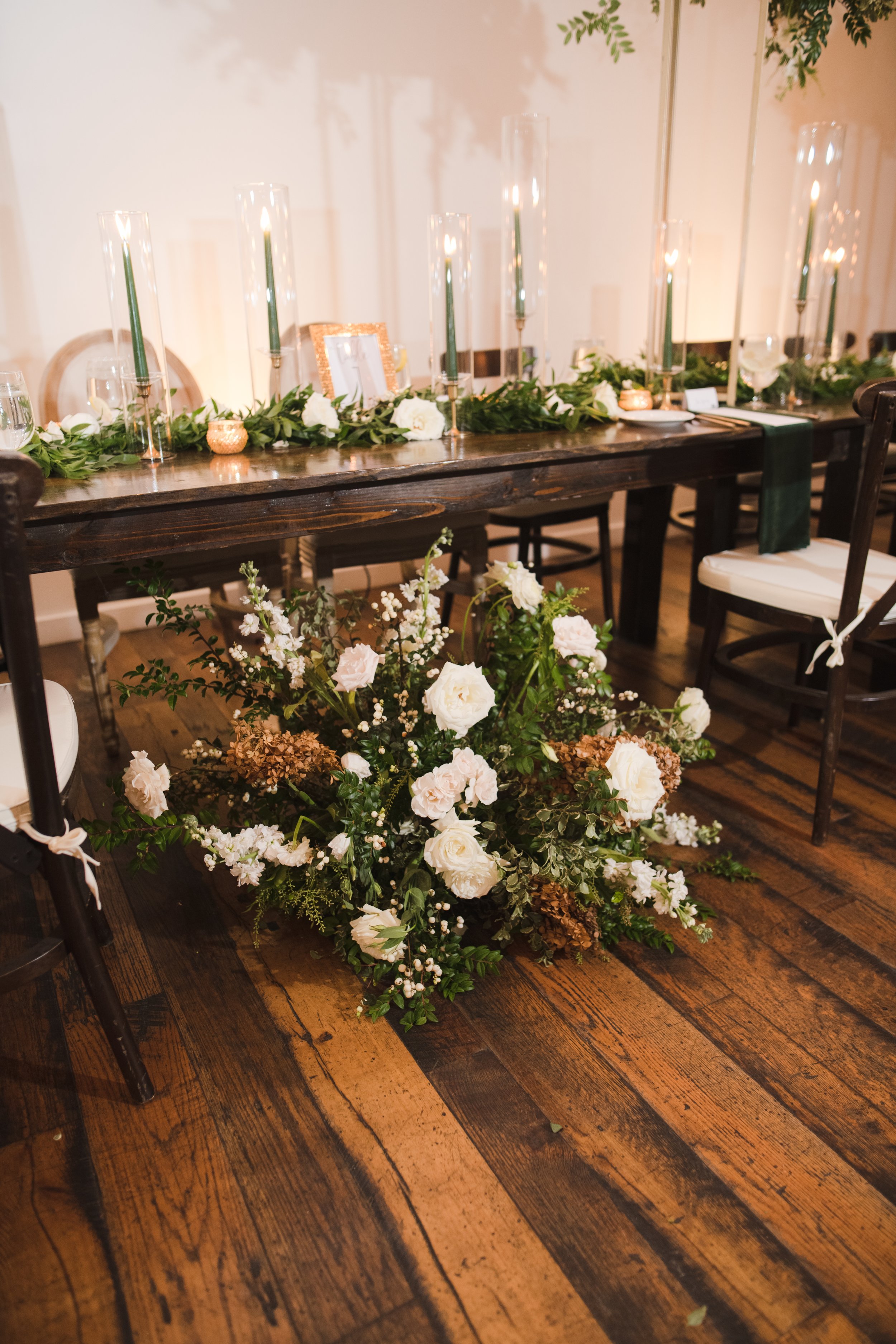 Elegant tablescapes for garden-inspired white and green wedding. Dark green tapers and natural garland. Accented with gold votives and petal heavy white roses. Designed by Rosemary and Finch in Nashville, TN.