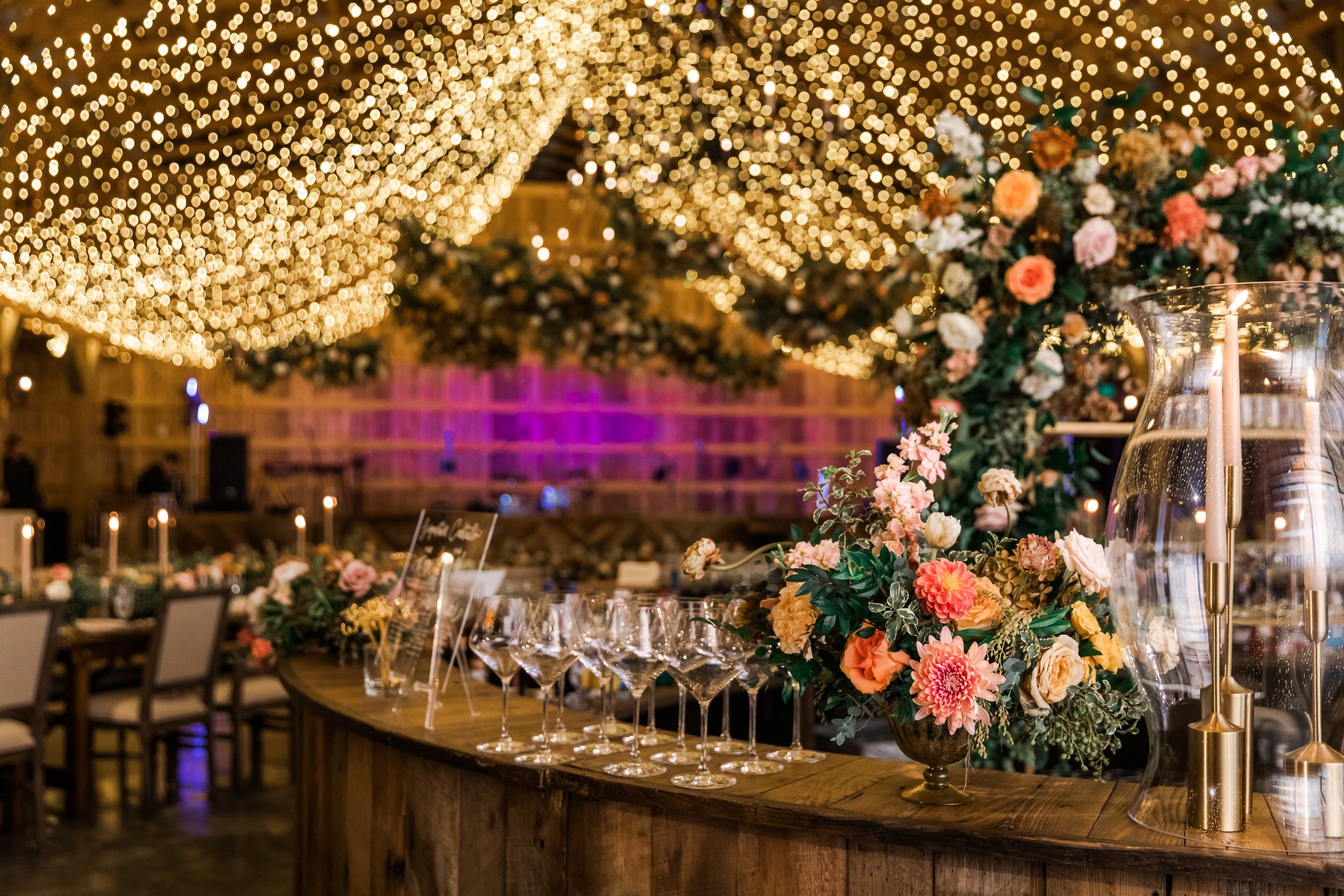Beautiful fall floral centerpieces warm this reception space with a sunset color palette. Garden roses, ranunculus, double brownie tulips, and lisianthus create hues of terra cotta, blush pink, copper, and yellow. Designed by Rosemary and Finch in Na
