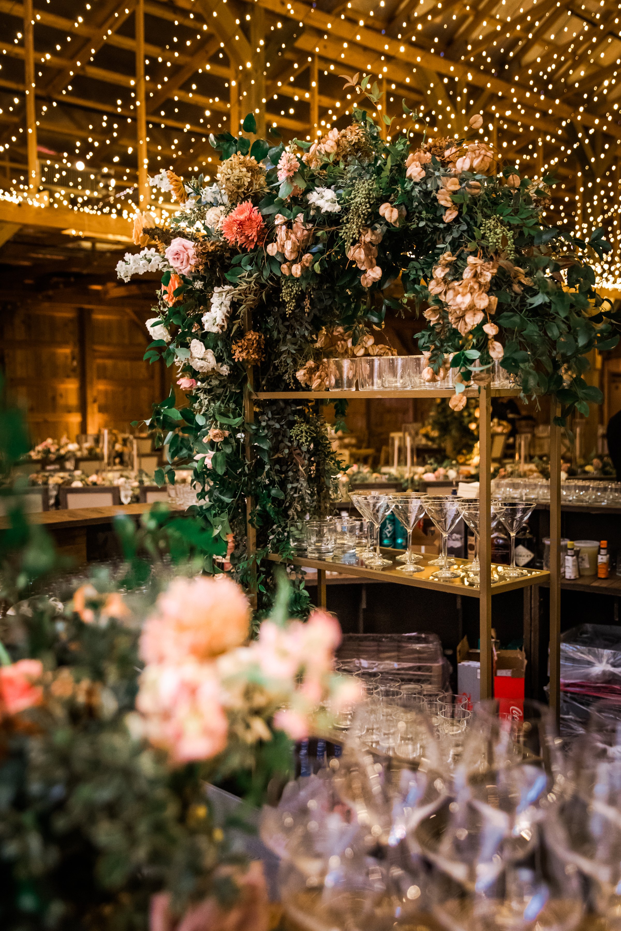 Stunning fall floral installation frame the bar area of this autumnal wedding. Hues of blush, terra cotta, copper, toffee, yellow, and other neutrals are highlighted with dahlias, roses, and double brownie tulips. Designed by Rosemary and Finch in Na