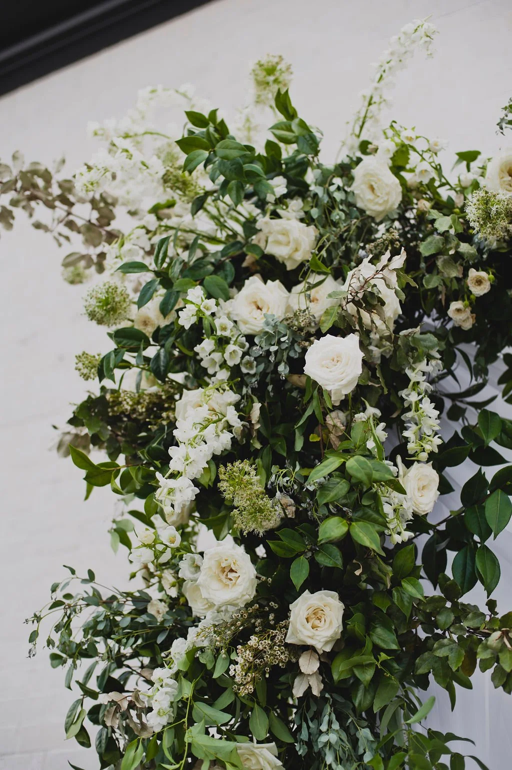A ceremony backdrop arch overflowing with garden roses, white ranunculus, spray roses, delphinium, spirea, greenery and smilax vine. Designed by Rosemary and Finch in Nashville, TN.