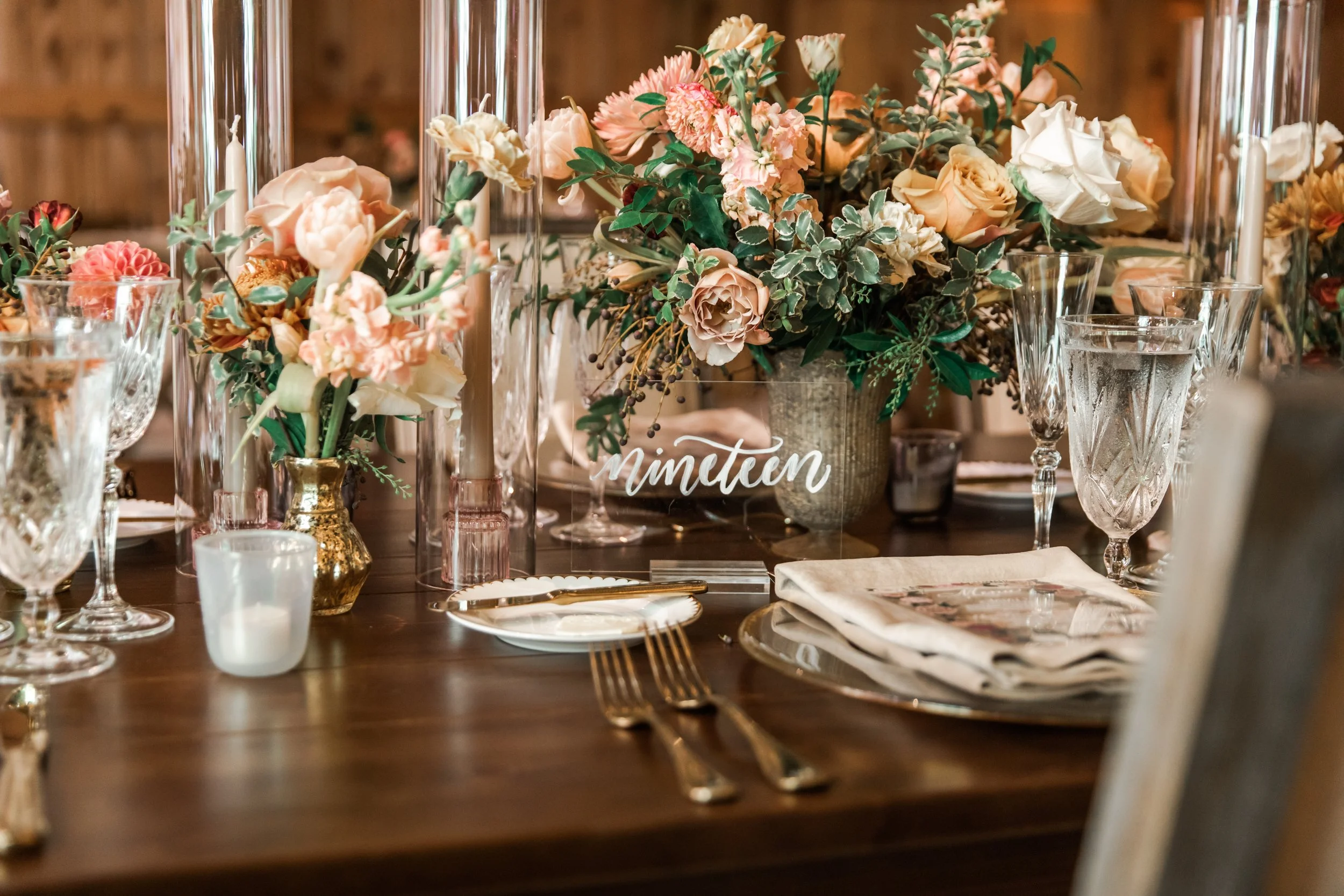 Beautiful fall floral centerpieces warm this reception space with a sunset color palette. Garden roses, ranunculus, double brownie tulips, and lisianthus create hues of terra cotta, blush pink, copper, and yellow. Designed by Rosemary and Finch in Na