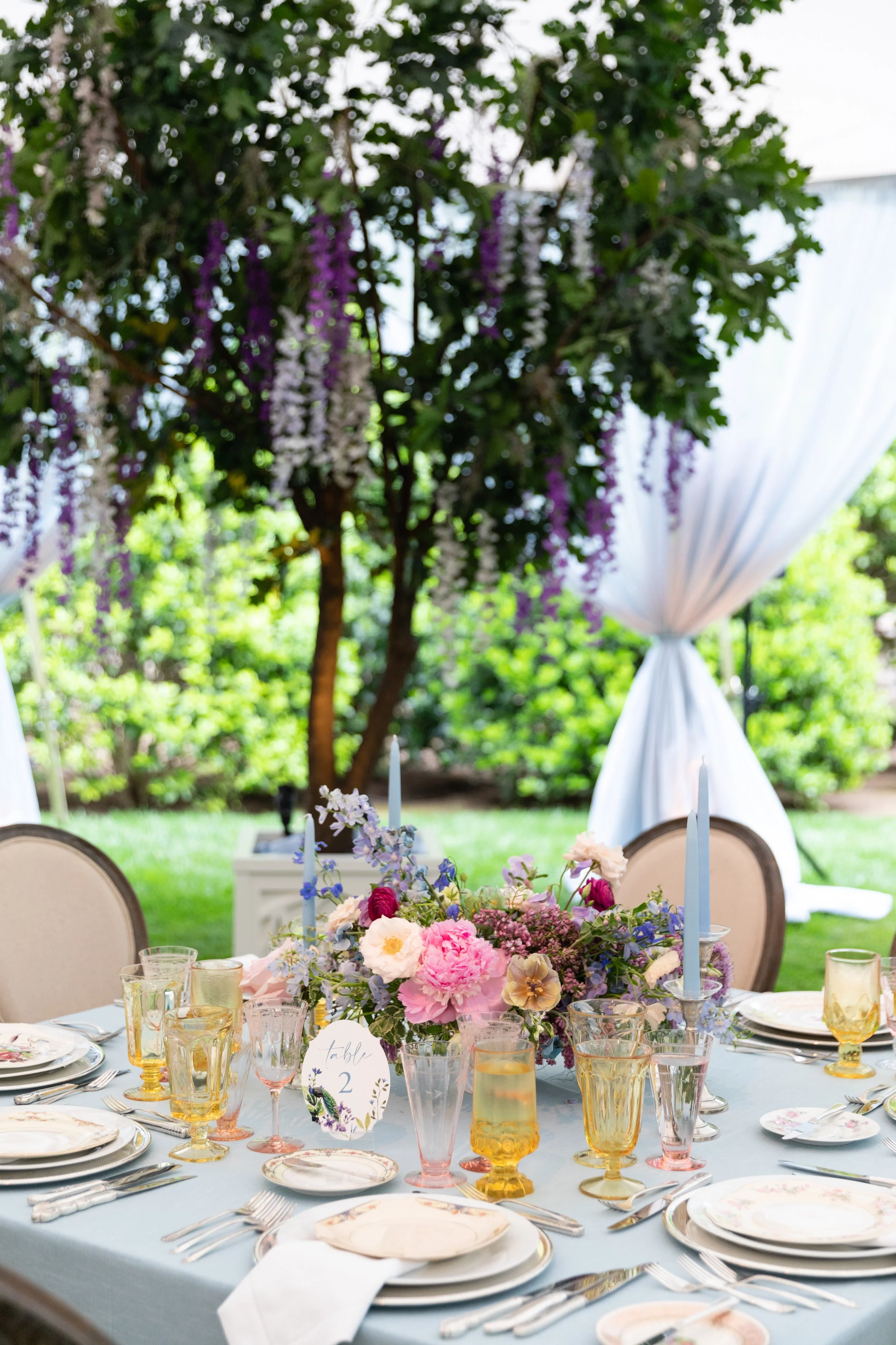 Growing, fresh floral centerpieces with blush garden roses, lilac, blue sweet peas, ranunculus, lavender delphinium, globe allium, and natural greenery for a tented Bridgerton inspired engagement party at a private home in Nashville, TN. Flower by Te
