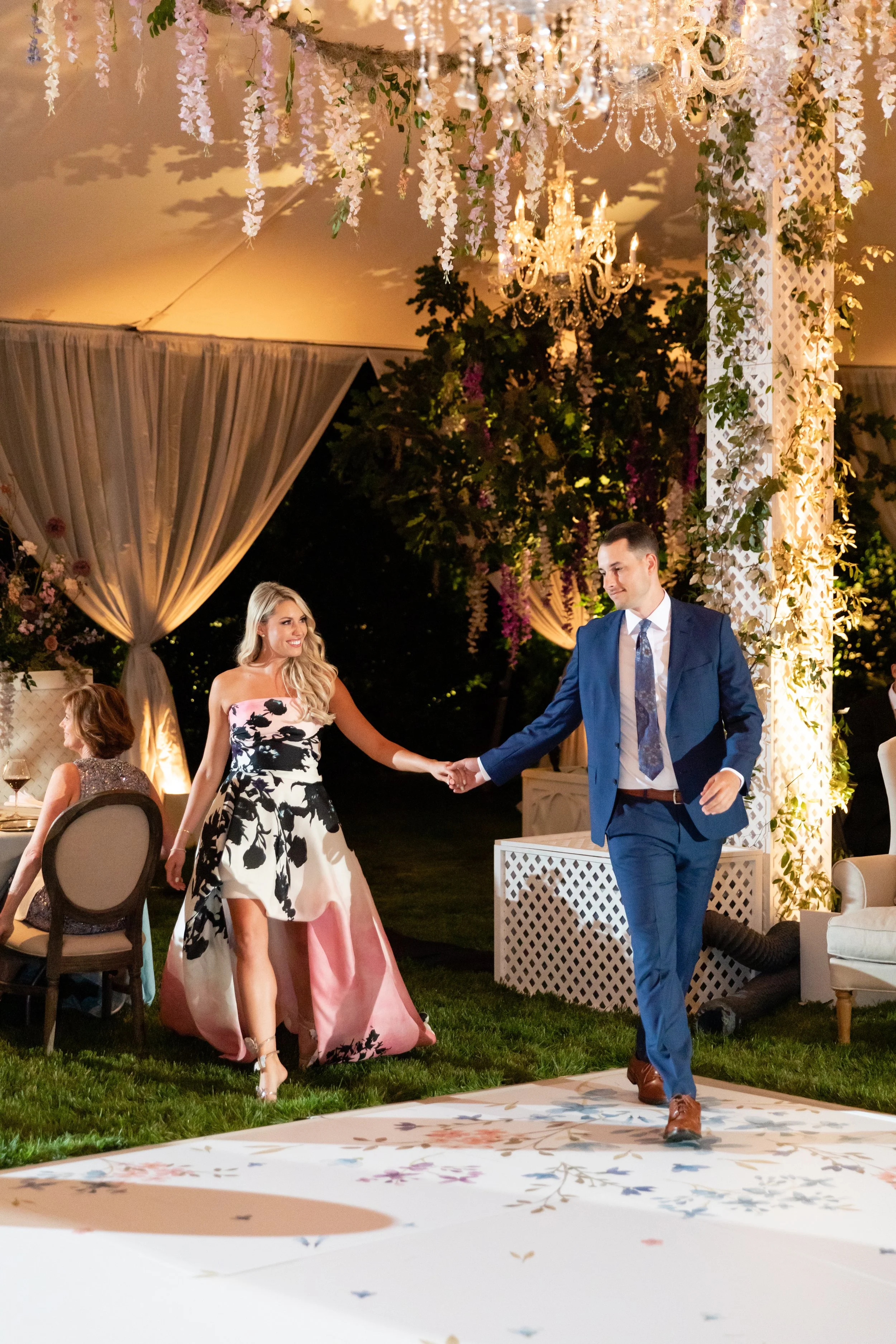 Growing, fresh floral installations and chandeliers with blush garden roses, lavender delphinium, wisteria, globe allium, and vines and greenery for a tented Bridgerton inspired engagement party at a private home in Nashville, TN.