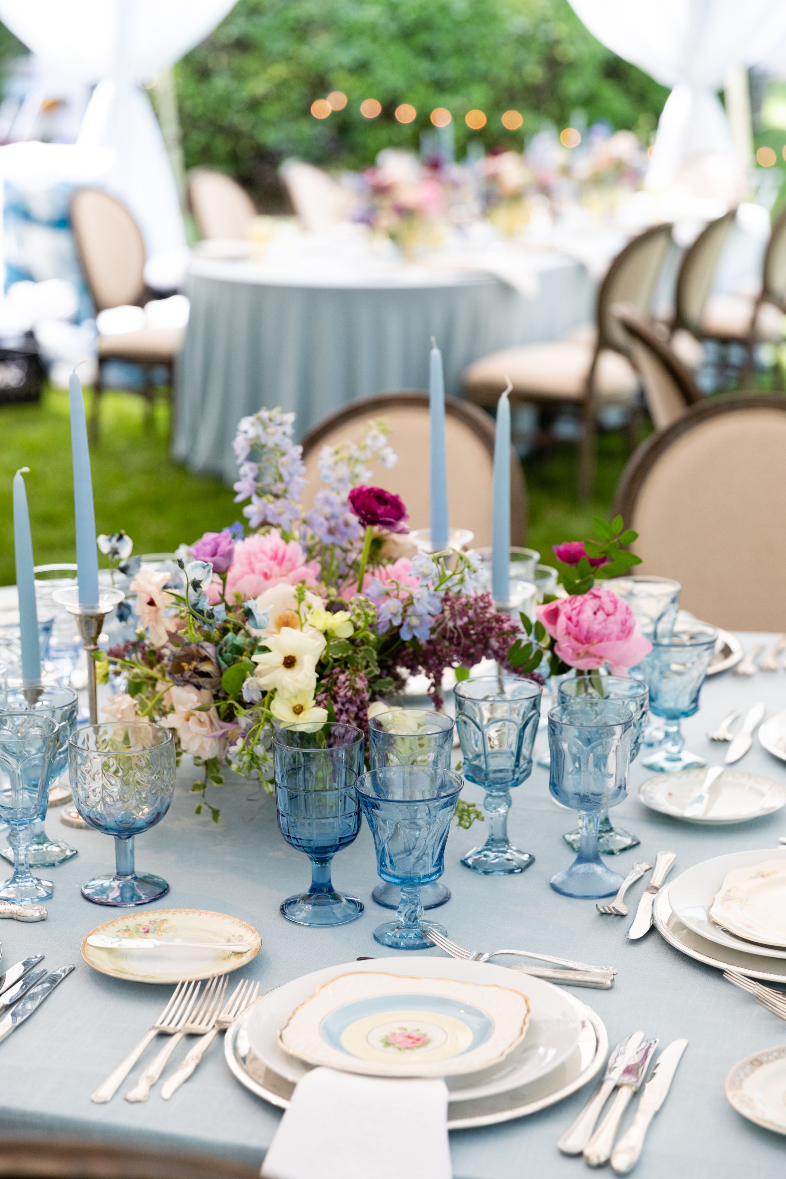Growing, fresh floral centerpieces with blush garden roses, lilac, blue sweet peas, ranunculus, lavender delphinium, globe allium, clematis, and natural greenery for a tented Bridgerton inspired engagement party at a private home in Nashville, TN.