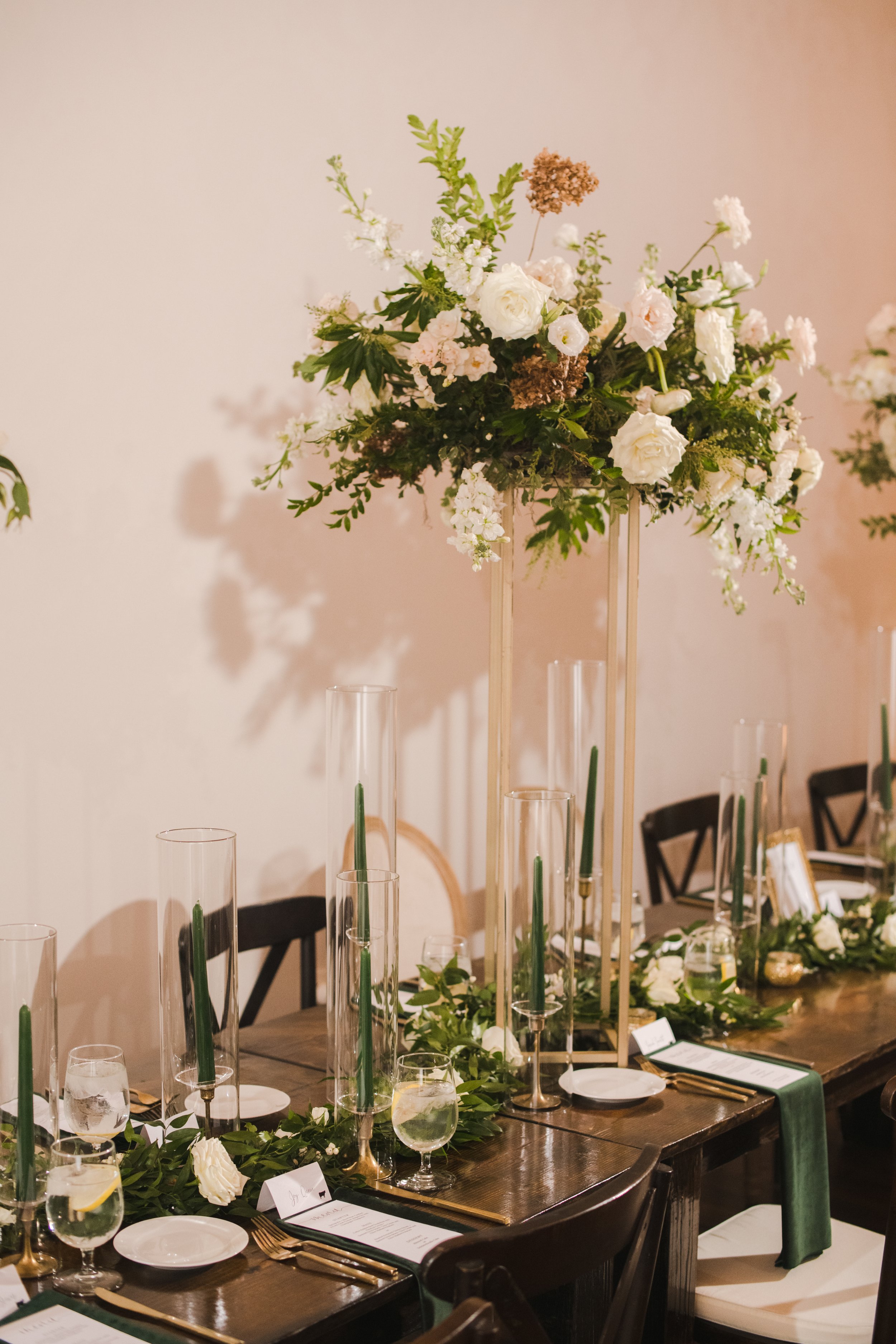 Elevated gold stands with lush floral centerpieces of white garden roses, ranunculus, snapdragons, and natural, untamed greenery. Designed by Rosemary and Finch in Nashville, TN.