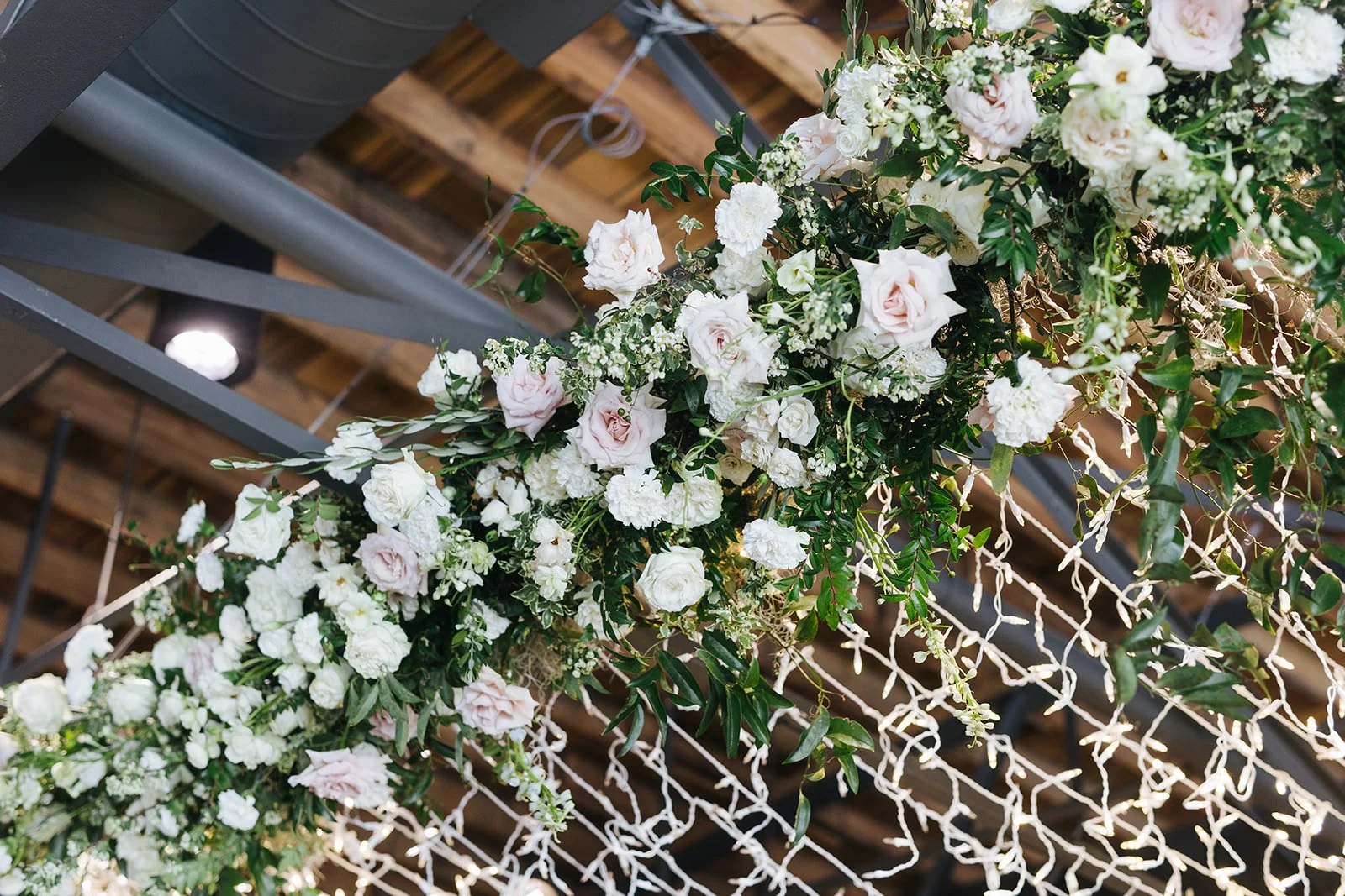 Lush floral chandelier lights up the dance floor with florals of petal heavy roses, ranunculus, lisianthus, delphinium, and dark greenery in hues of white, cream, and blush. Designed by Rosemary and Finch in Nashville, TN.