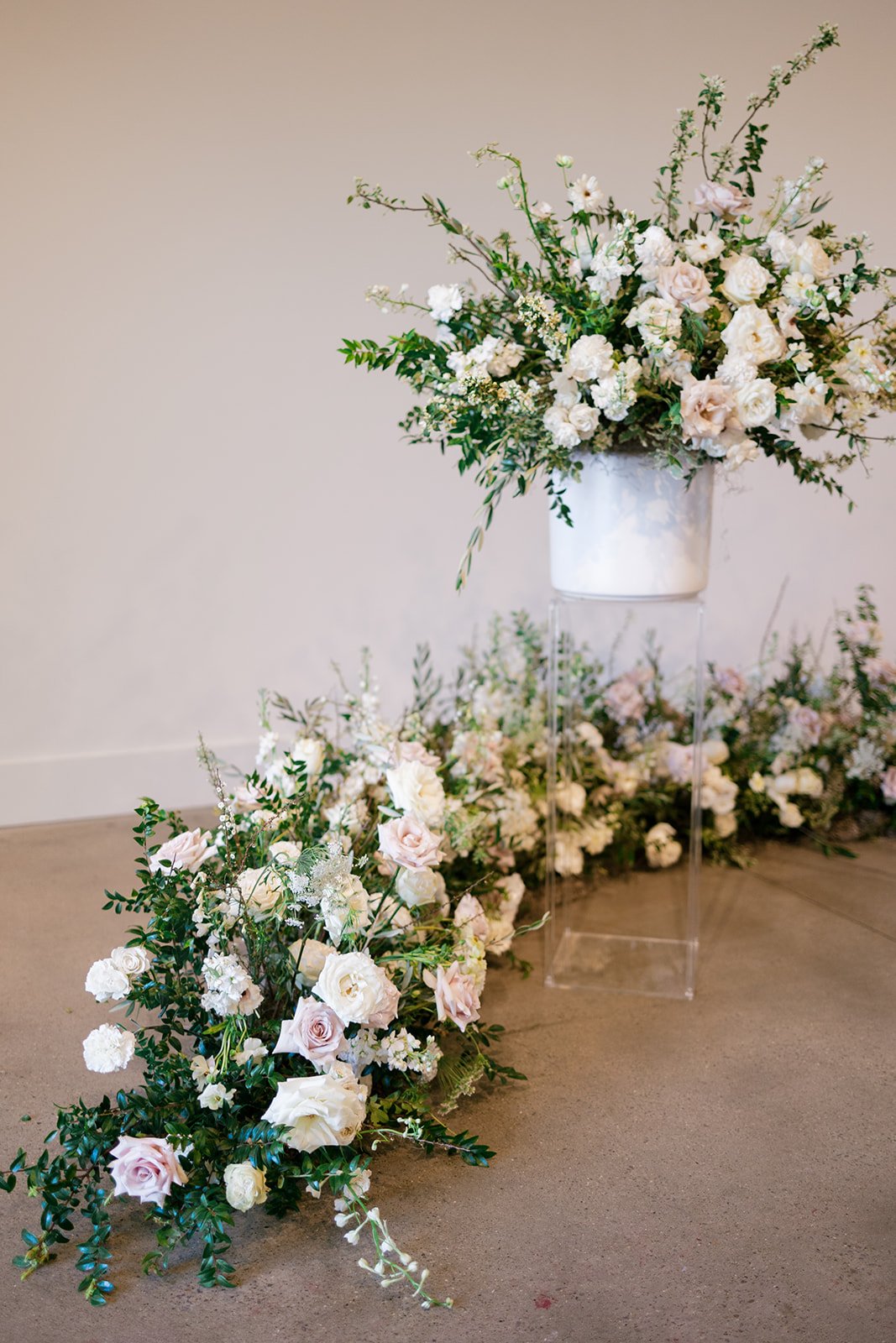 Lush ceremony installation featuring garden urns and meadows with petal heavy roses butterfly ranunculus, delphinium, and Queen Anne’s lace with natural, untamed greenery. Floral hues of white, cream, and blush. Designed by Rosemary and Finch in Nash