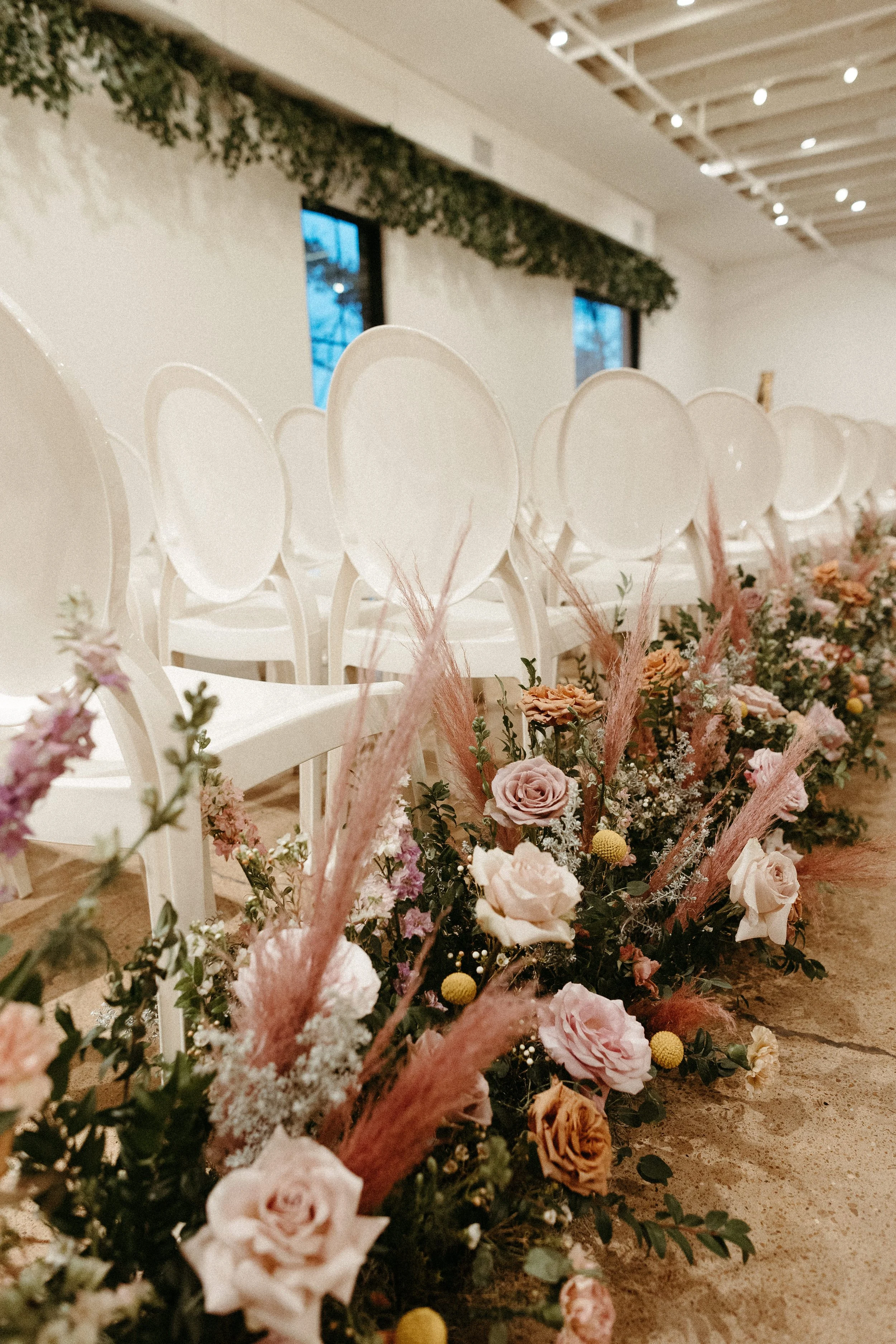 Lush aisle meadows beautifully frame the ceremony of this winter wedding with hues of dusty pink, terra cotta, cream, and sage green. Complete with petal heavy roses and pink pampas grass. Designed by Rosemary and Finch in Nashville, TN.