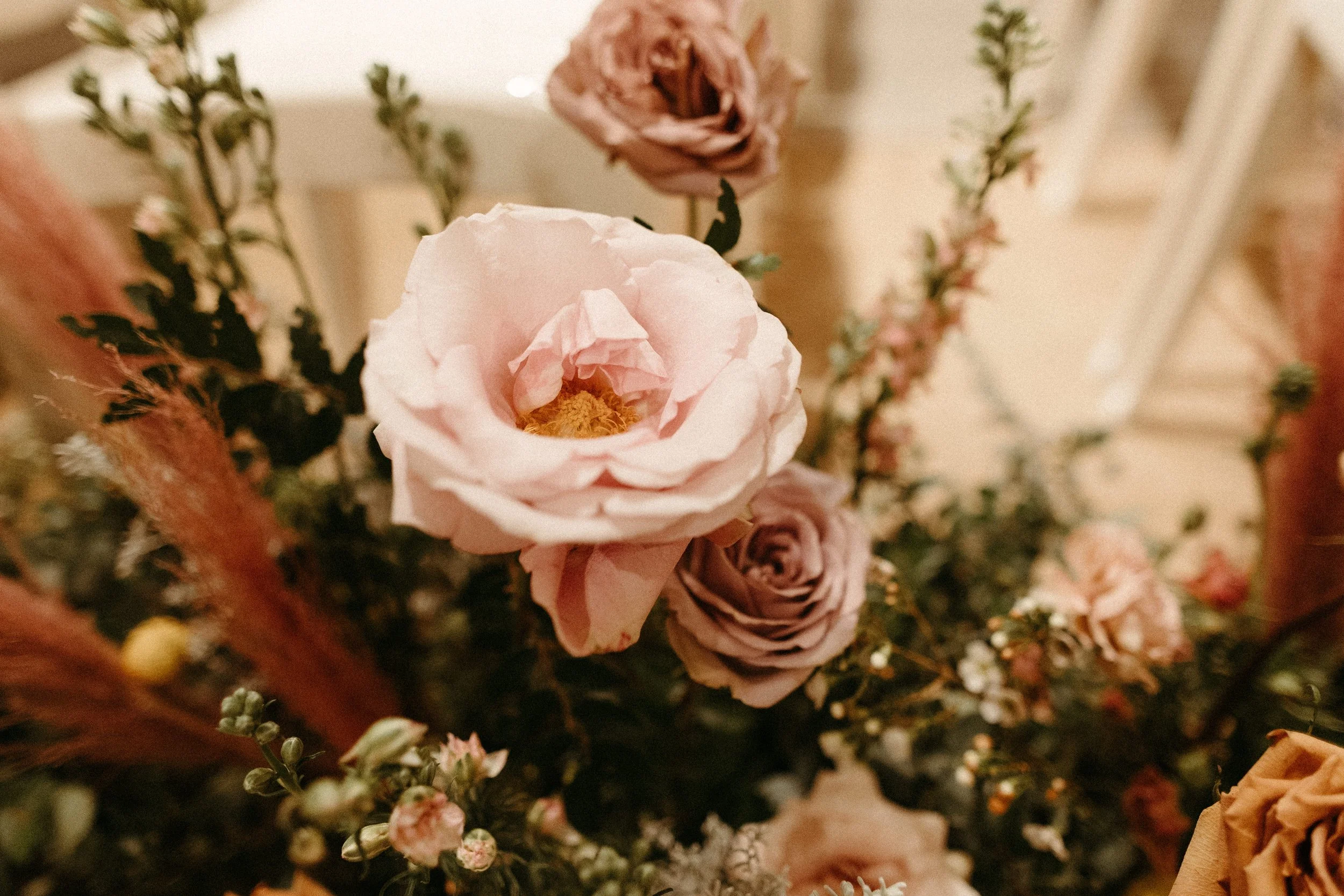 Lush aisle meadows beautifully frame the ceremony of this winter wedding with hues of dusty pink, terra cotta, cream, and sage green. Complete with petal heavy roses and pink pampas grass. Designed by Rosemary and Finch in Nashville, TN.