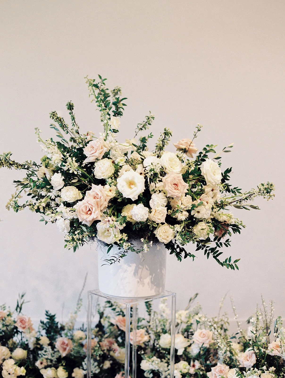 Lush ceremony installation featuring garden urns and meadows with petal heavy roses butterfly ranunculus, delphinium, and Queen Anne’s lace with natural, untamed greenery. Floral hues of white, cream, and blush. Designed by Rosemary and Finch in Nash