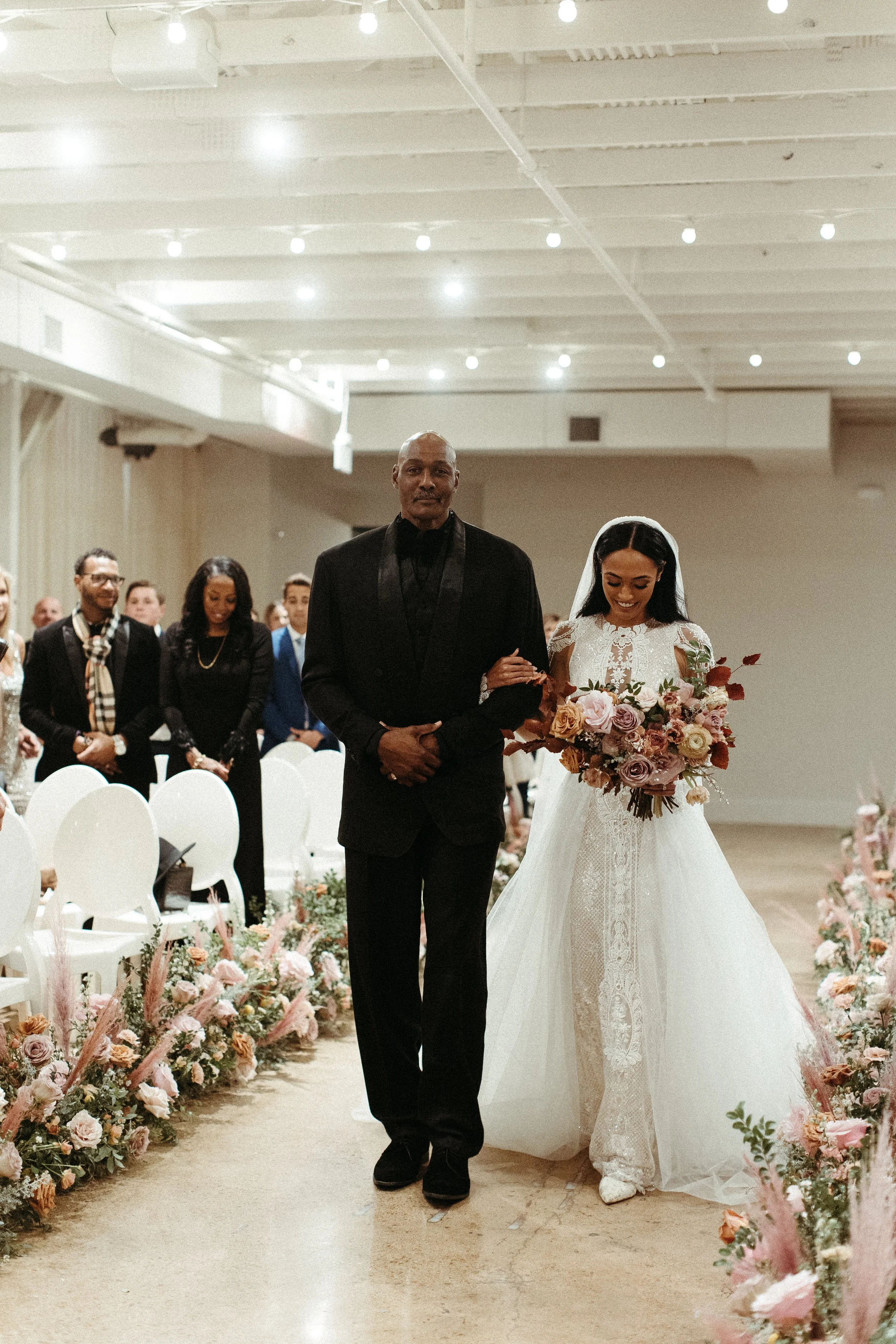 Lush aisle meadows beautifully frame the ceremony of this winter wedding with hues of dusty pink, terra cotta, cream, and sage green. Complete with petal heavy roses and pink pampas grass. Designed by Rosemary and Finch in Nashville, TN.