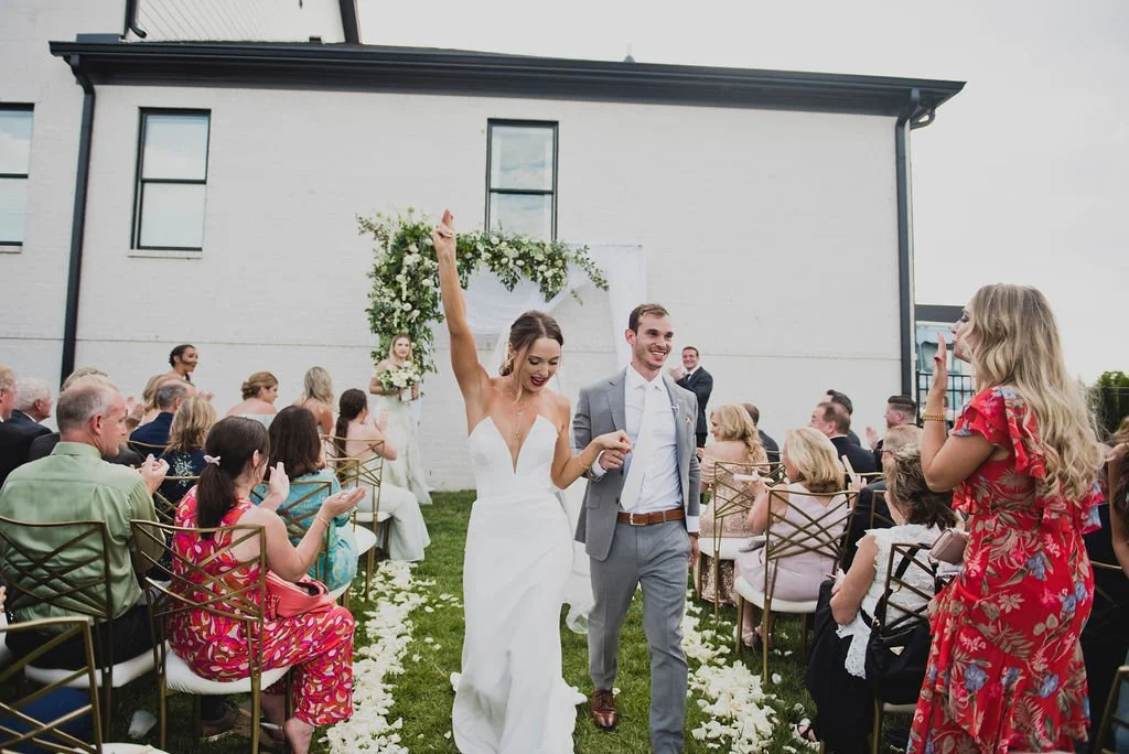 A ceremony backdrop arch overflowing with garden roses, white ranunculus, spray roses, delphinium, spirea, greenery and smilax vine. Designed by Rosemary and Finch in Nashville, TN.