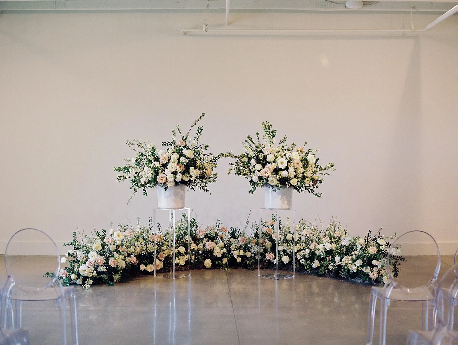 Lush ceremony installation featuring garden urns and meadows with petal heavy roses butterfly ranunculus, delphinium, and Queen Anne’s lace with natural, untamed greenery. Floral hues of white, cream, and blush. Designed by Rosemary and Finch in Nash