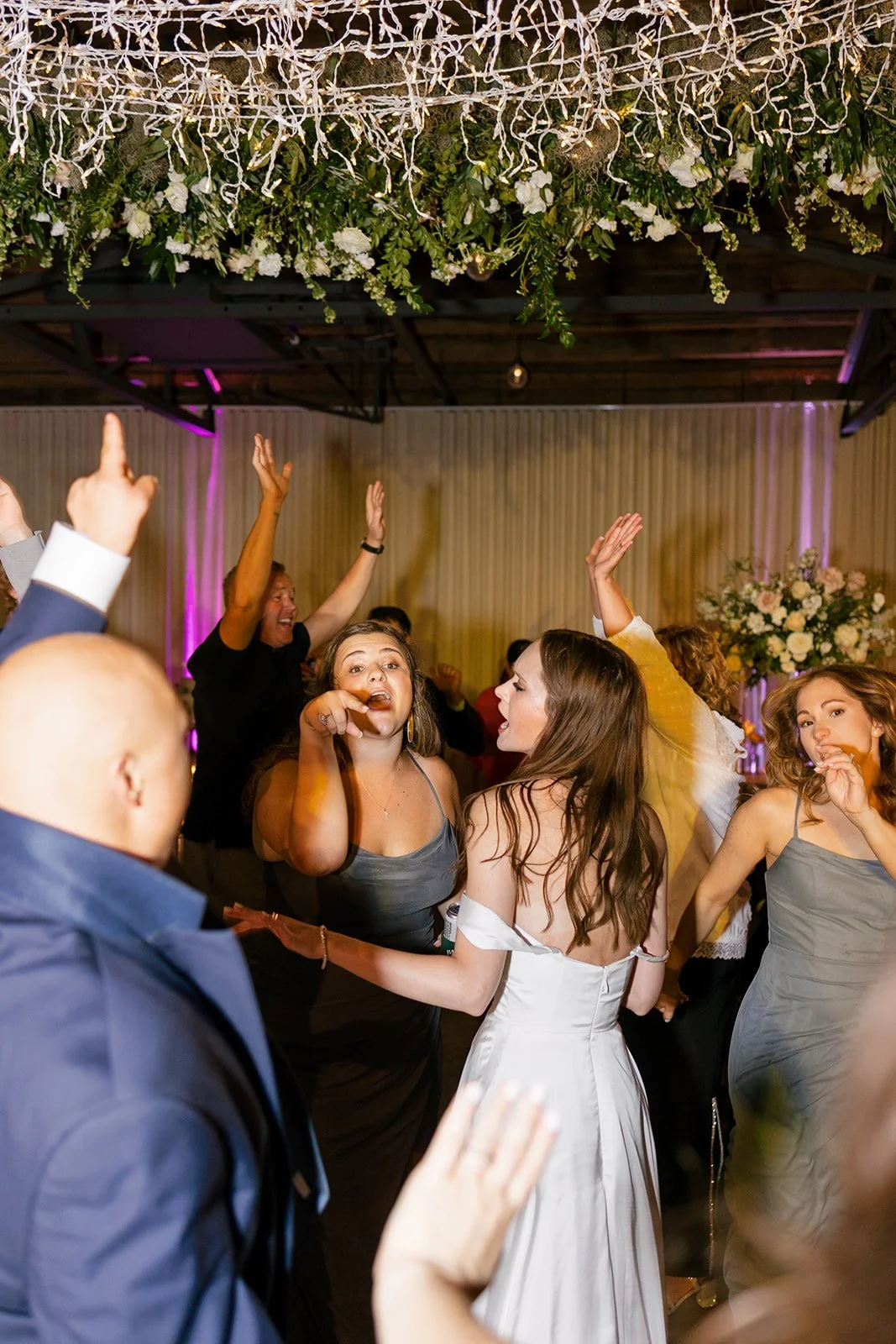 Lush floral chandelier lights up the dance floor with florals of petal heavy roses, ranunculus, lisianthus, delphinium, and dark greenery in hues of white, cream, and blush. Designed by Rosemary and Finch in Nashville, TN.