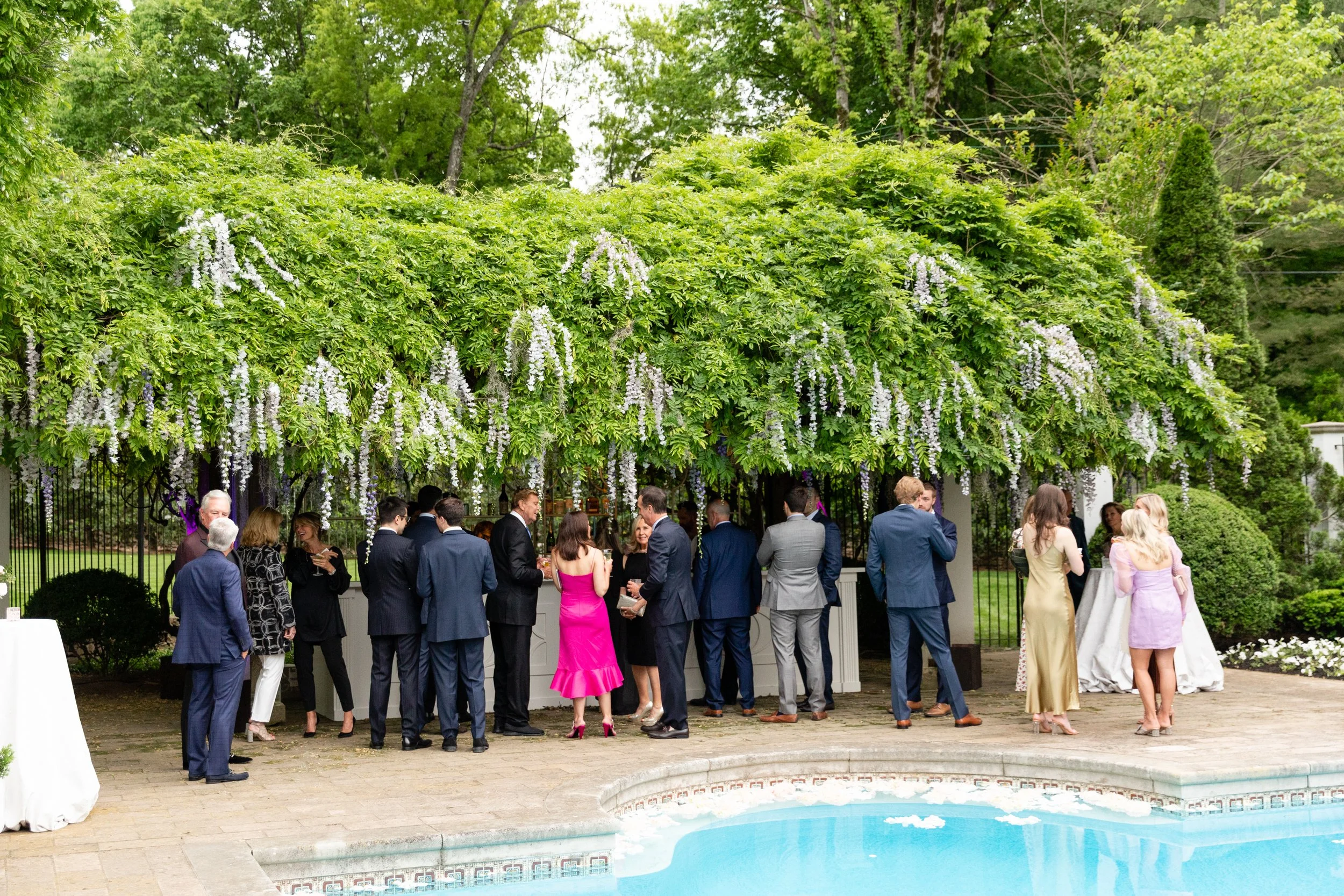 Bridgerton inspired engagement party at a private home in Nashville, TN with pastel candles and flowers floating in the pool with wisteria and delphinium growing over the bar. Nashville wedding floral designer, Rosemary & Finch.
