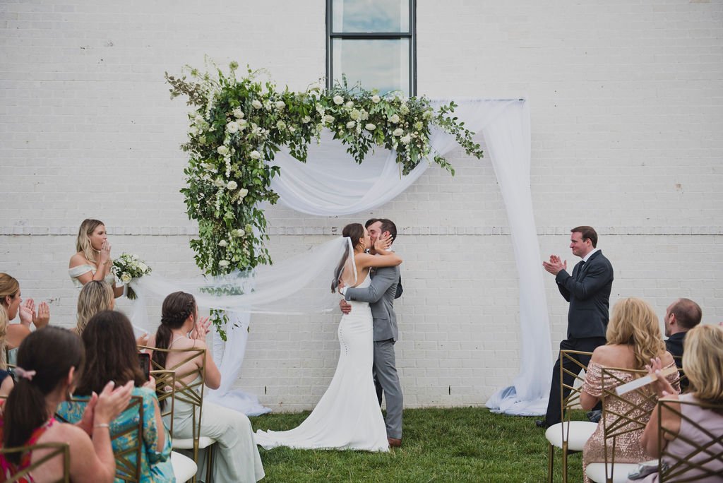 A ceremony backdrop arch overflowing with garden roses, white ranunculus, spray roses, delphinium, spirea, greenery and smilax vine. Designed by Rosemary and Finch in Nashville, TN.
