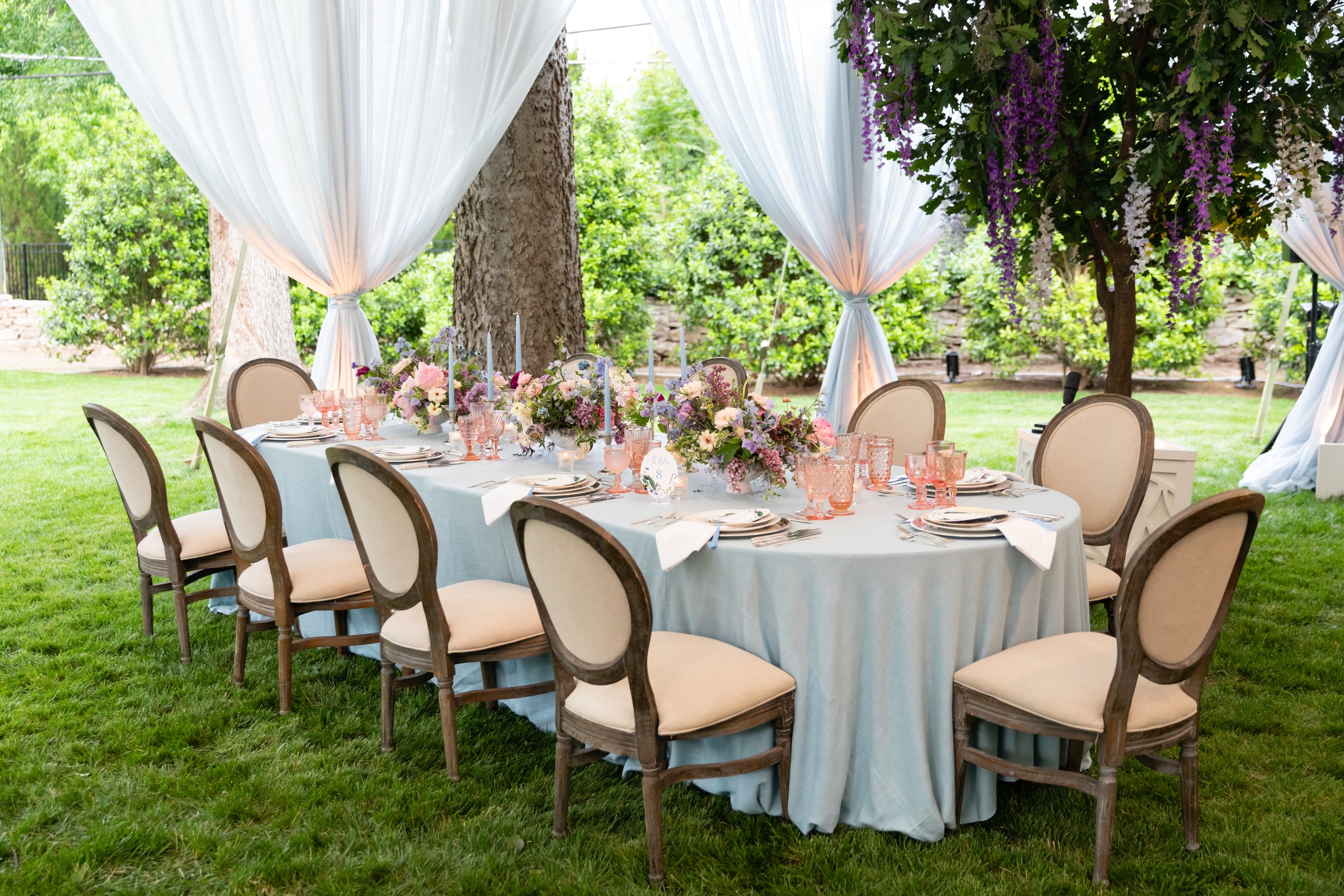 Growing, fresh floral installations and chandeliers with blush garden roses, lavender delphinium, wisteria, globe allium, and vines and greenery for a tented Bridgerton inspired engagement party at a private home in Nashville, TN.