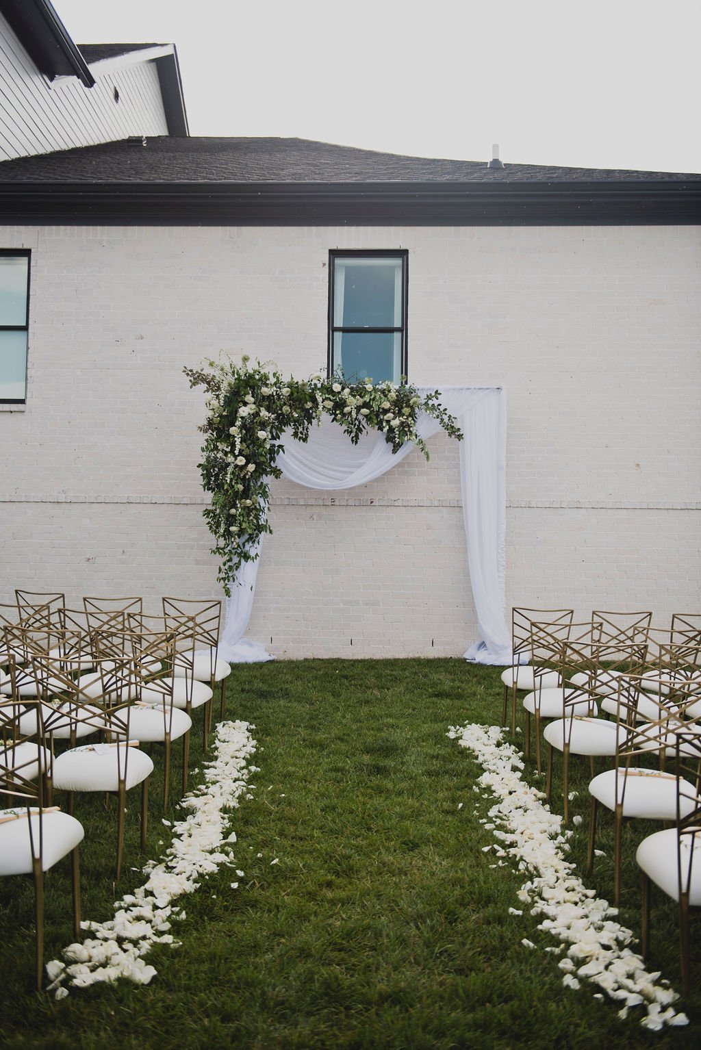 A ceremony backdrop arch overflowing with garden roses, white ranunculus, spray roses, delphinium, spirea, greenery and smilax vine. Rose petals line the aisle. Designed by Rosemary and Finch in Nashville, TN.