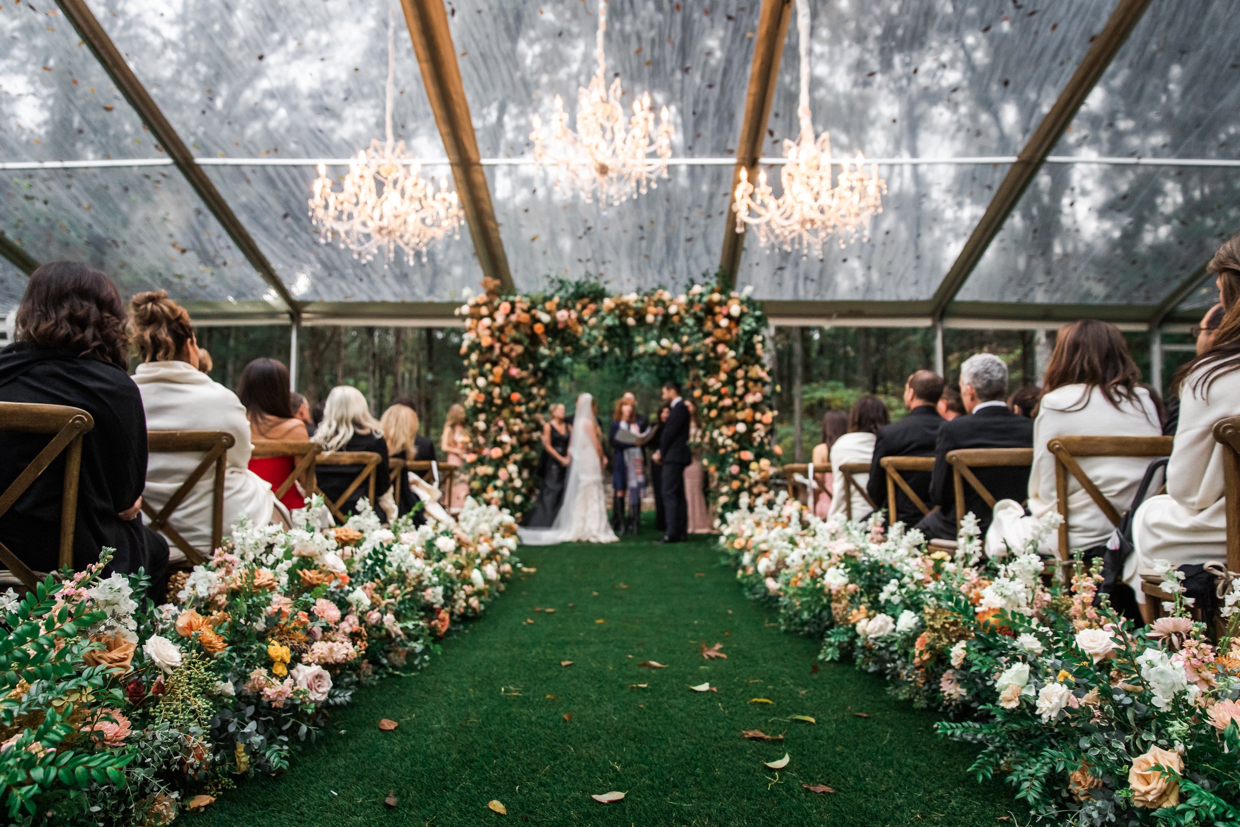 Lush floral hedges create aisle meadows for this fall wedding. Florals feature hues of terra cotta, blush, yellow, copper, and neutrals. Beautiful garden roses, dahlias, and fall florals highlight these arrangements. Design by Rosemary and Finch in N