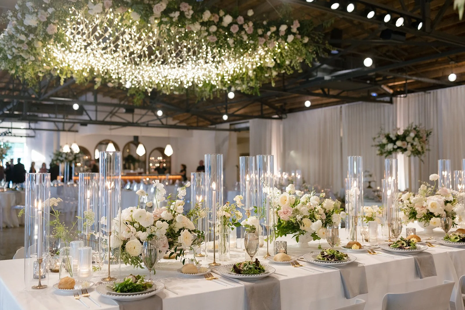 Low floral centerpieces for elegant wedding overflowing with white garden roses, ranunculus, butterfly ranunculus, scabiosa, lisianthus, sweet peas, and natural dark greenery. Floral hues of white, cream, and blush. Designed by Rosemary and Finch in