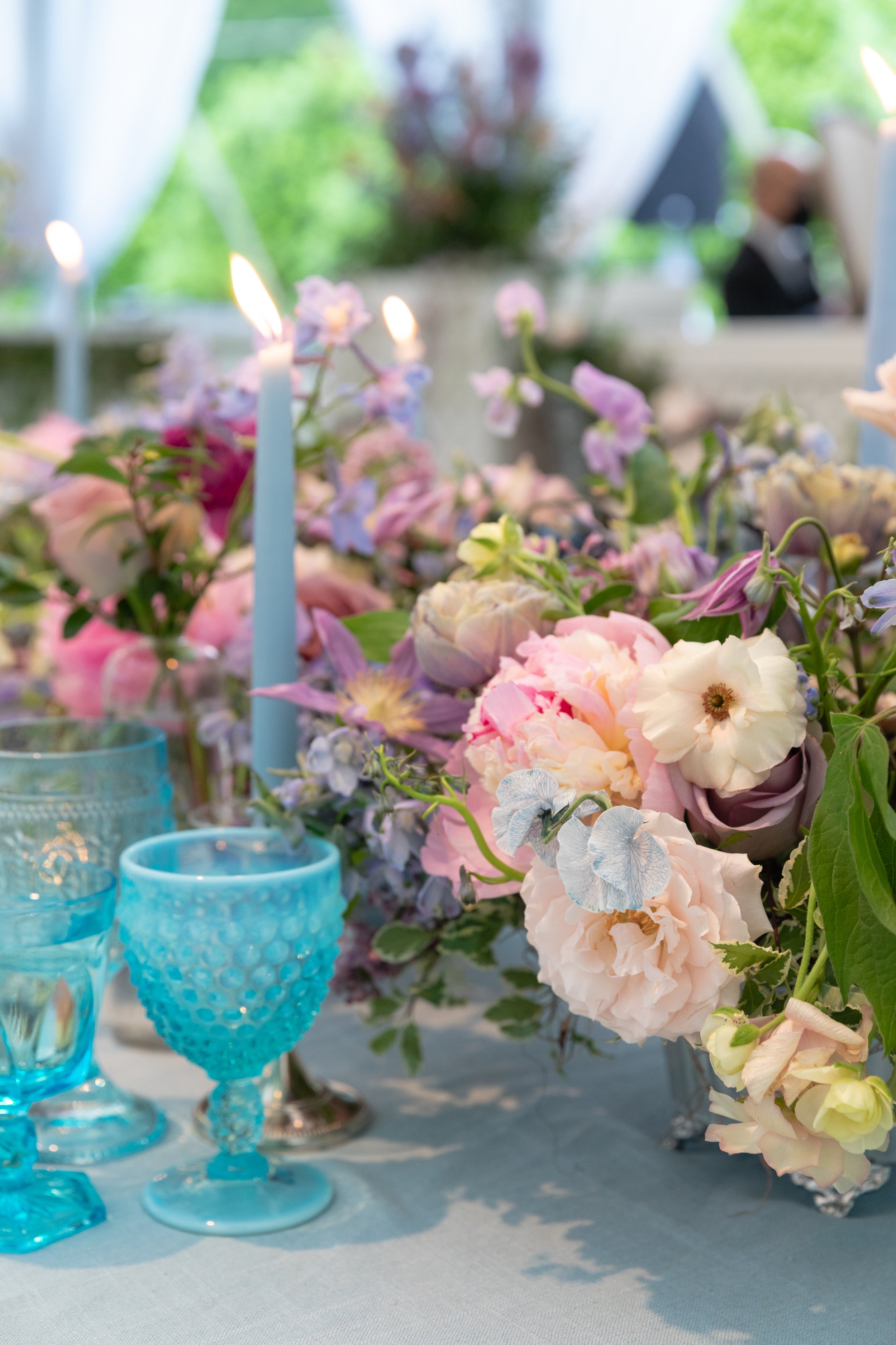 Growing, fresh floral centerpieces with blush garden roses, lilac, blue sweet peas, ranunculus, lavender delphinium, globe allium, clematis, and natural greenery for a tented Bridgerton inspired engagement party at a private home in Nashville, TN. Fl