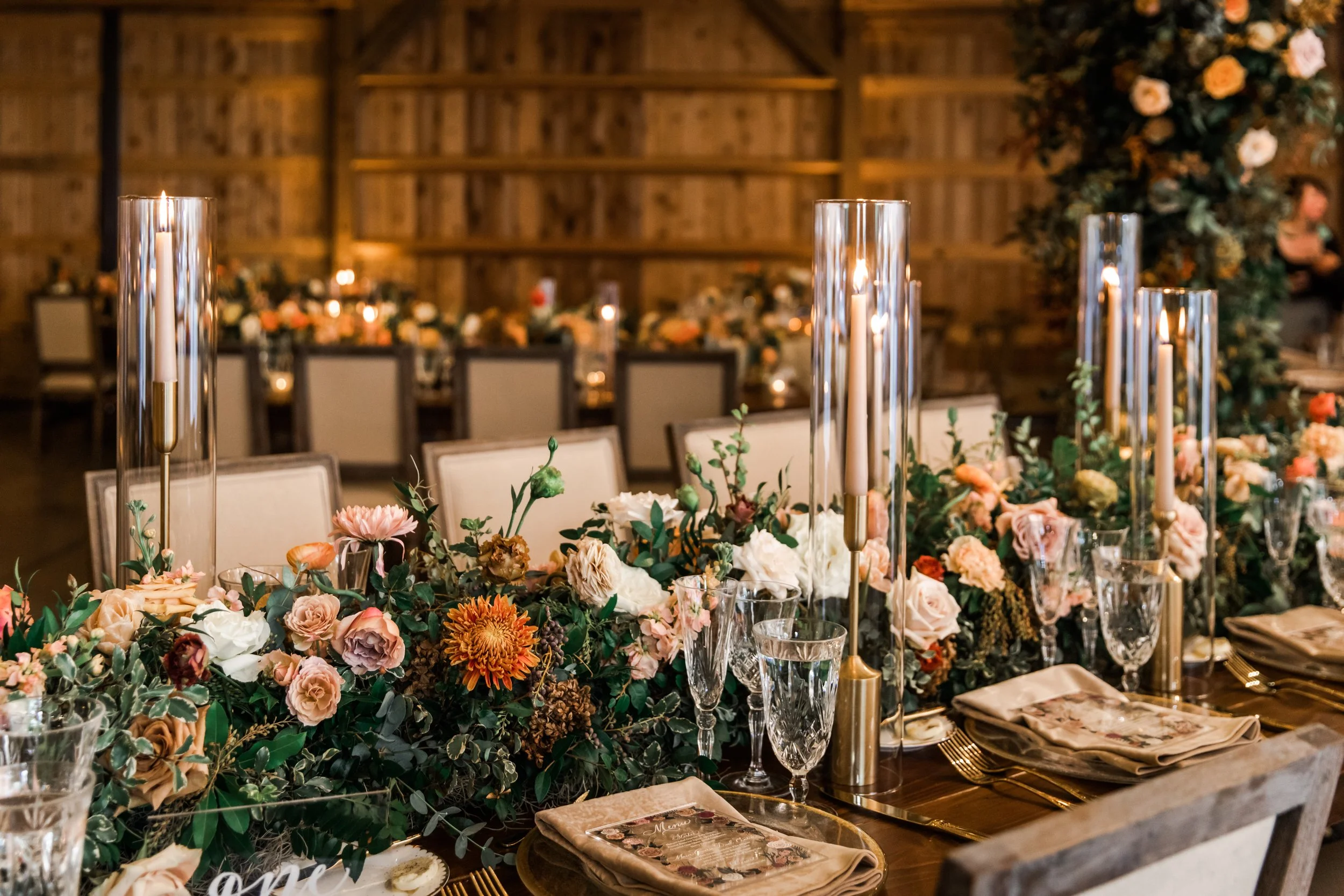 Stunning floral cascades line tables of this fall reception with terra cotta, blush, yellow hues, and taupe taper candles. Florals featuring dahlias, roses, and rain tree pods create lush arrangements. Designed by Rosemary and Finch in Nashville, TN.