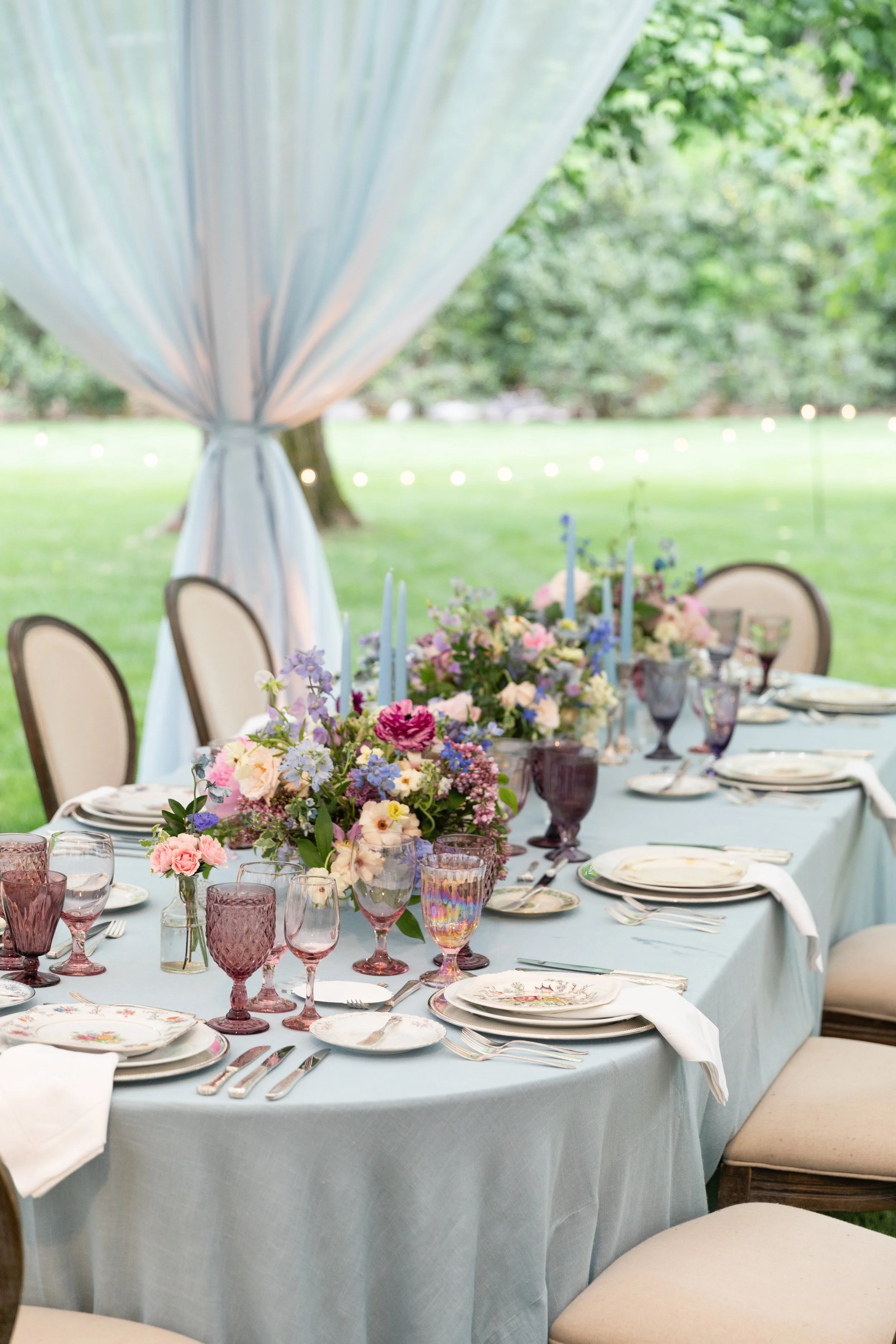 Growing, fresh floral centerpieces with blush garden roses, lilac, blue sweet peas, ranunculus, lavender delphinium, globe allium, and natural greenery for a tented Bridgerton inspired engagement party at a private home in Nashville, TN. Flower by Te