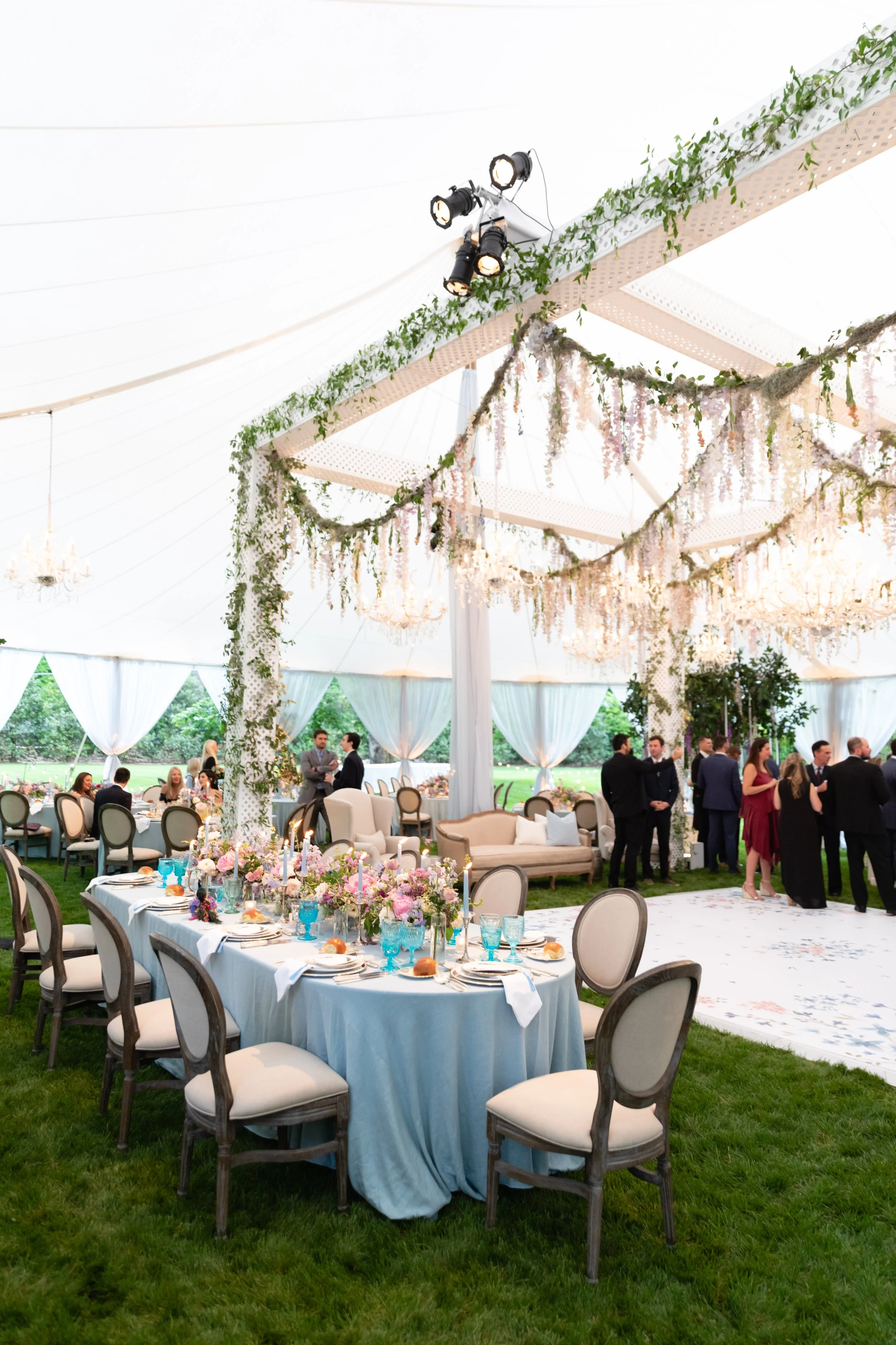 Growing, fresh floral installations with blush garden roses, lavender delphinium, wisteria, globe allium, and vines and greenery for a tented Bridgerton inspired engagement party at a private home in Nashville, TN. Flower by Tennessee based wedding f